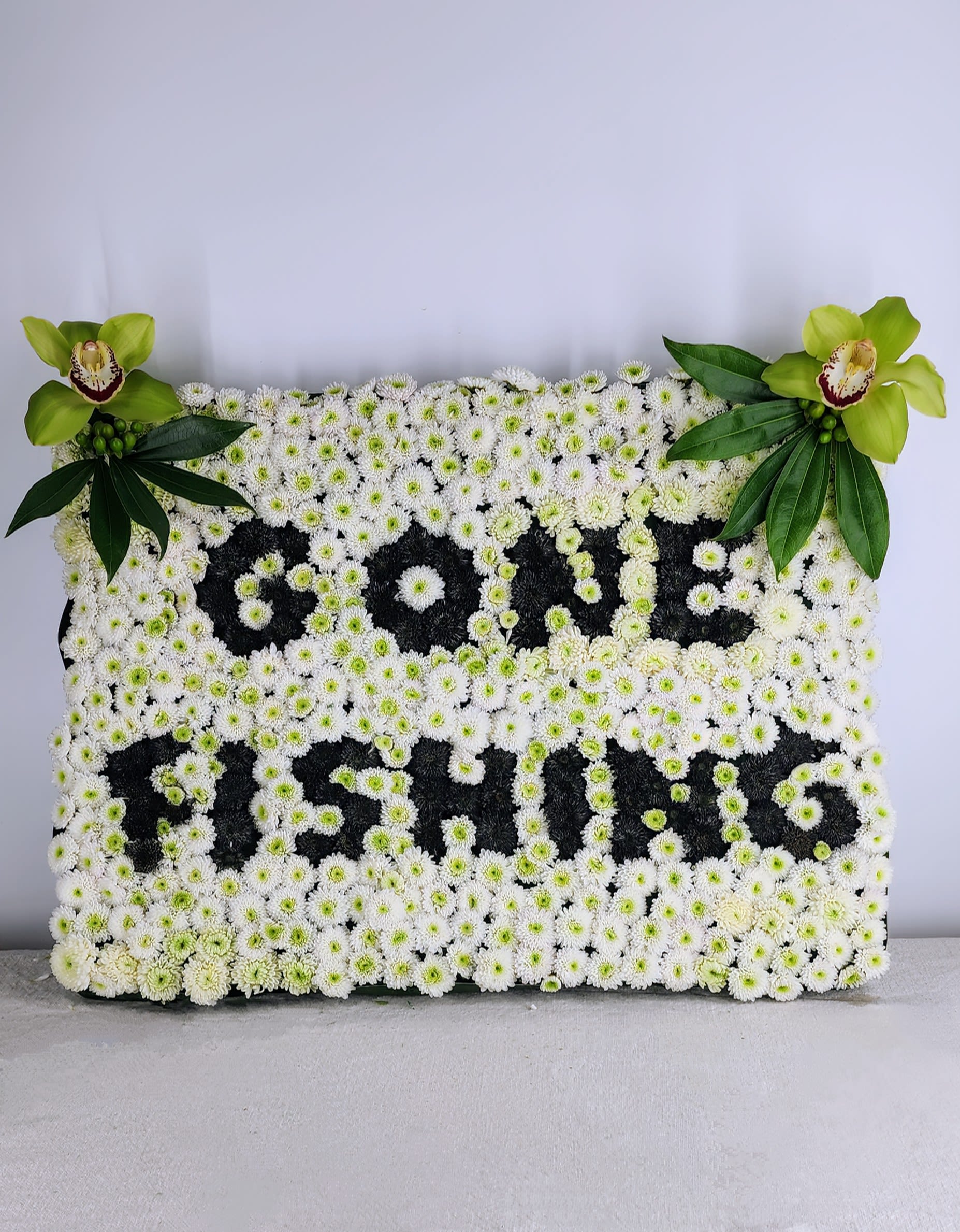 White floral tribute with green orchids and leaves spelling "PAPA"