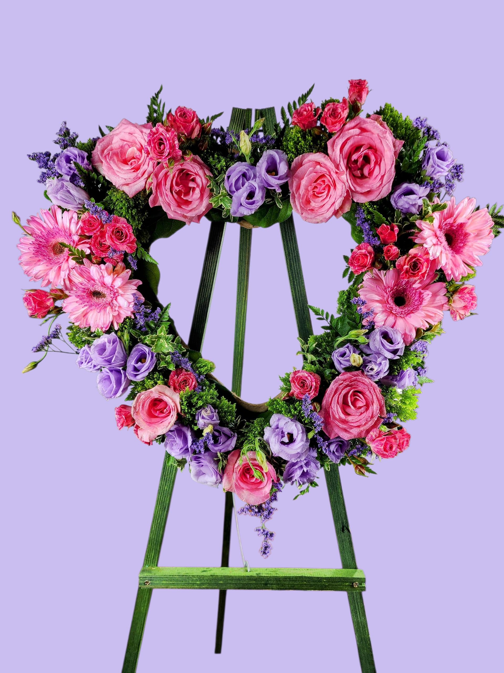 Heart-shaped floral wreath on a green easel with pink and purple flowers