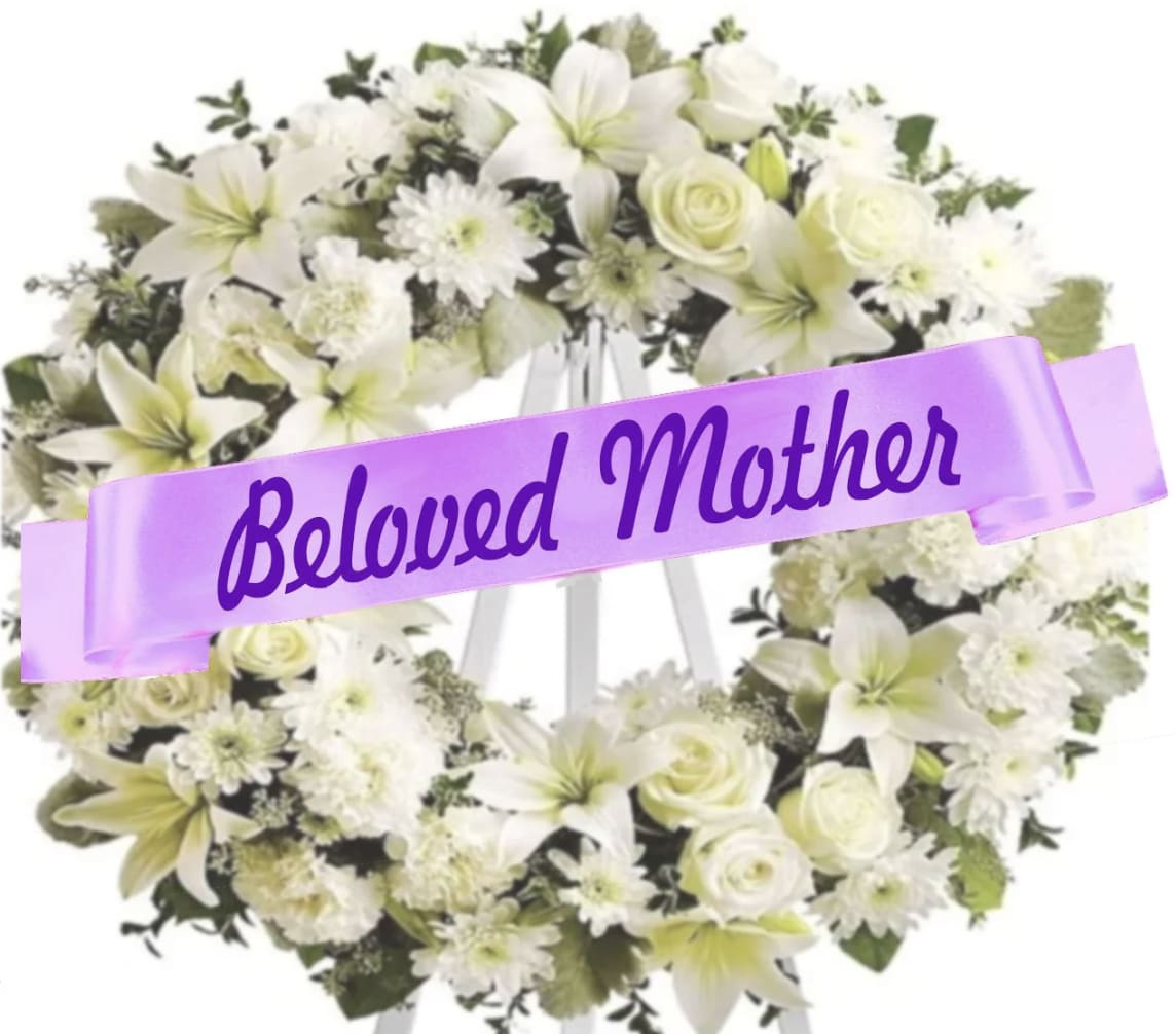 White floral wreath on an easel with a purple ribbon reading Beloved Mother