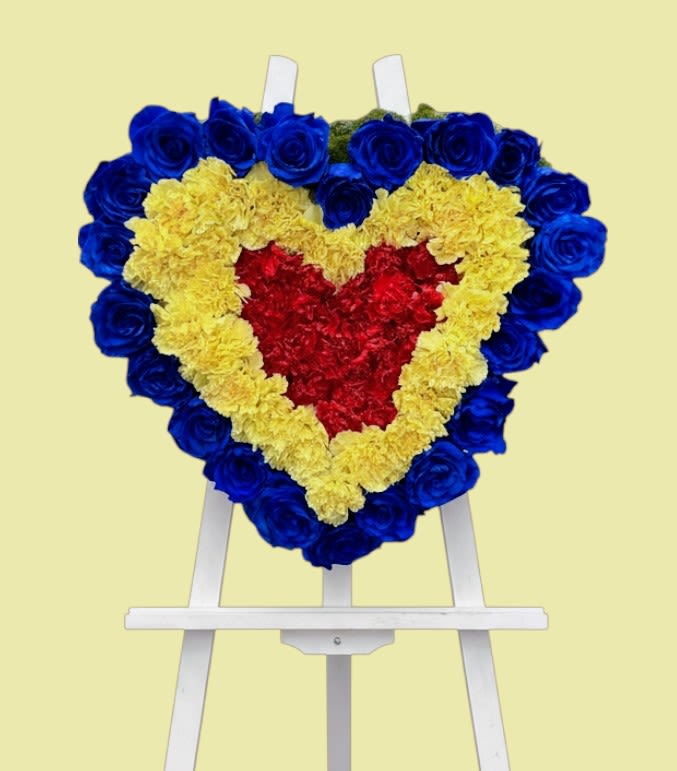 Heart-shaped floral wreath on a white easel with blue, yellow, and red flowers