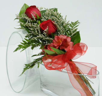 Red roses and pink flowers with a red ribbon in a clear vase