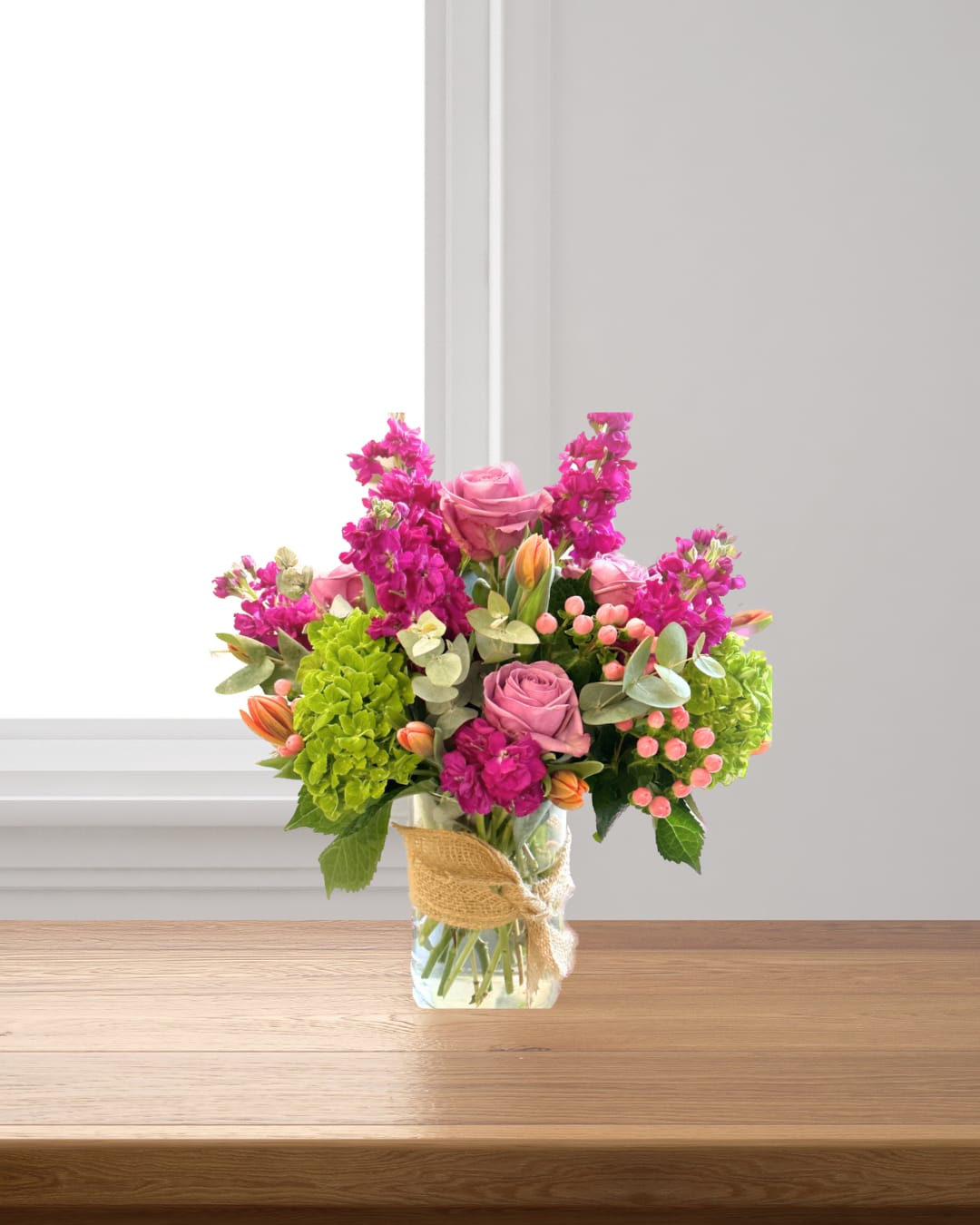 Pink roses and magenta flowers in a glass vase with burlap ribbon