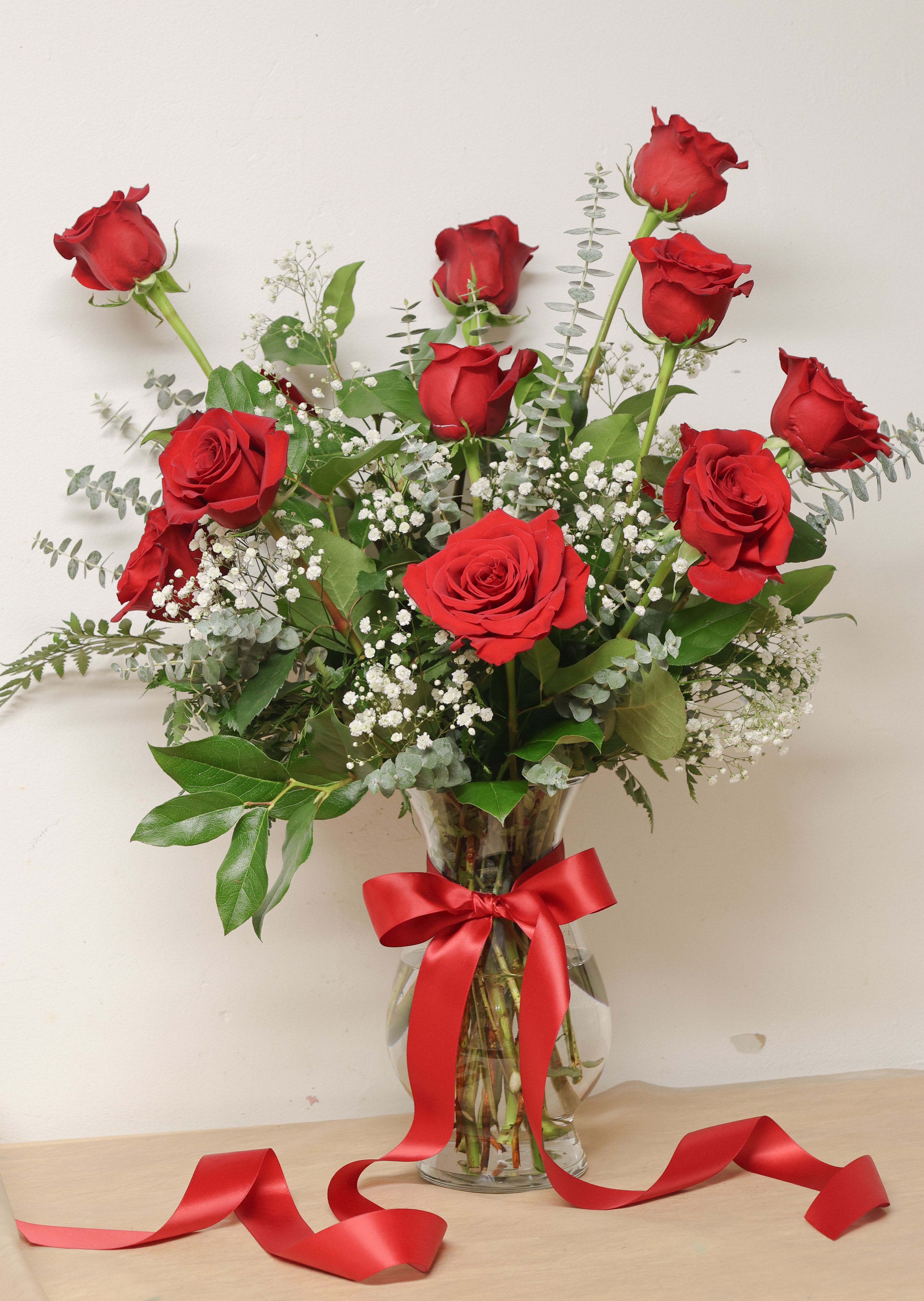 Red roses arranged in a clear glass vase with a red ribbon.