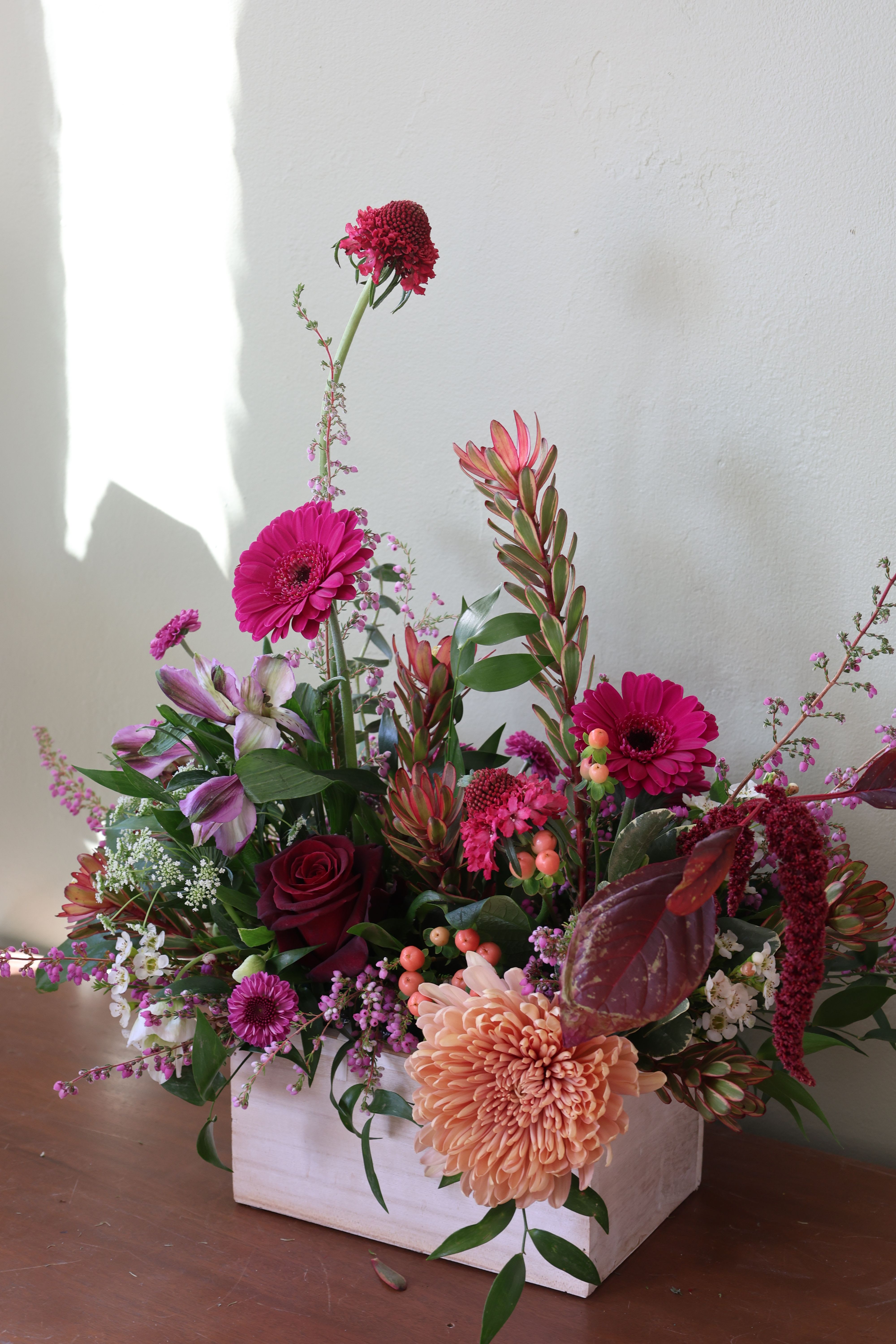 Mixed floral arrangement in a white wooden box with pink and peach blooms