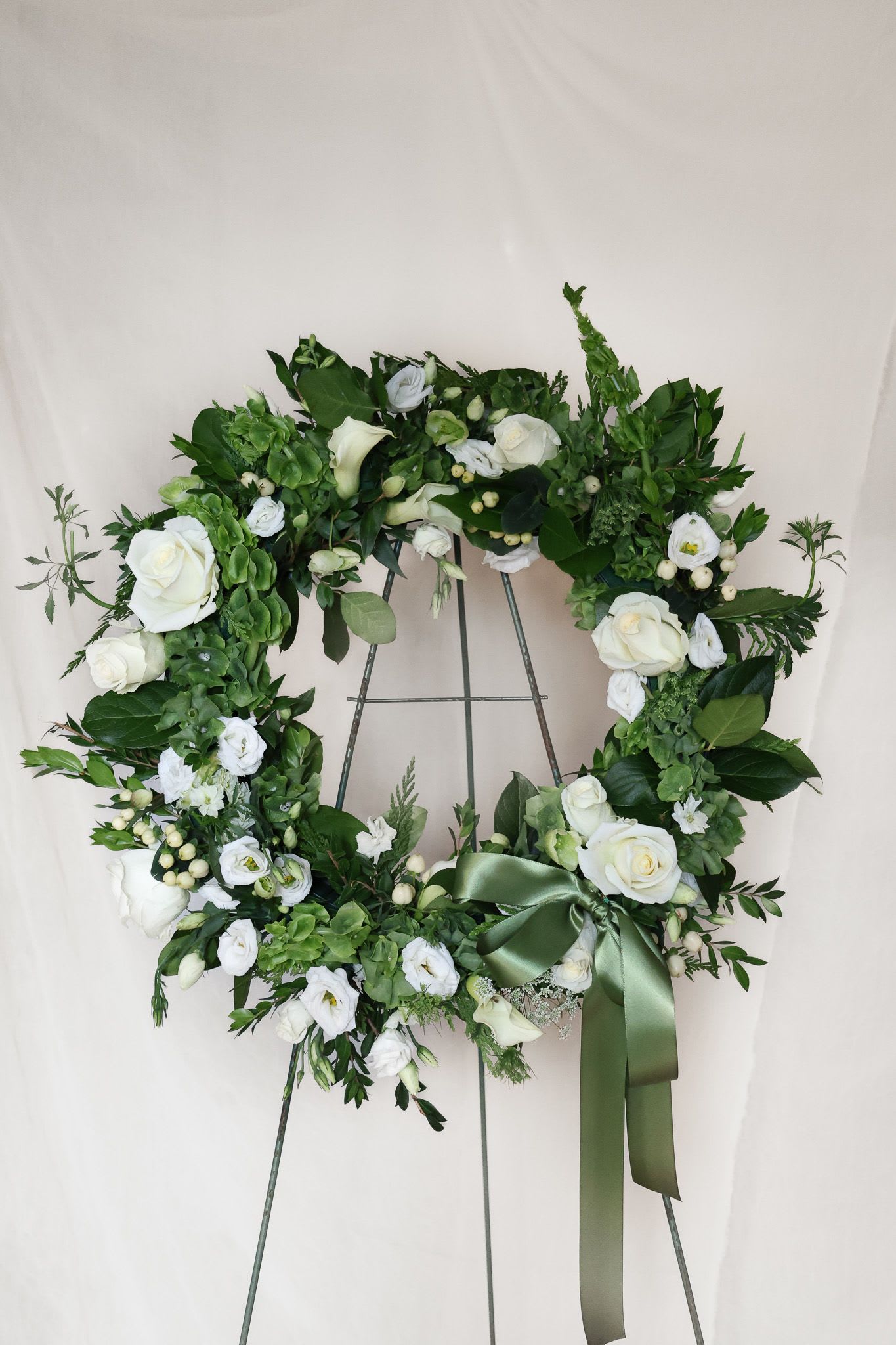 White rose and calla lily wreath on a metal stand with a green ribbon