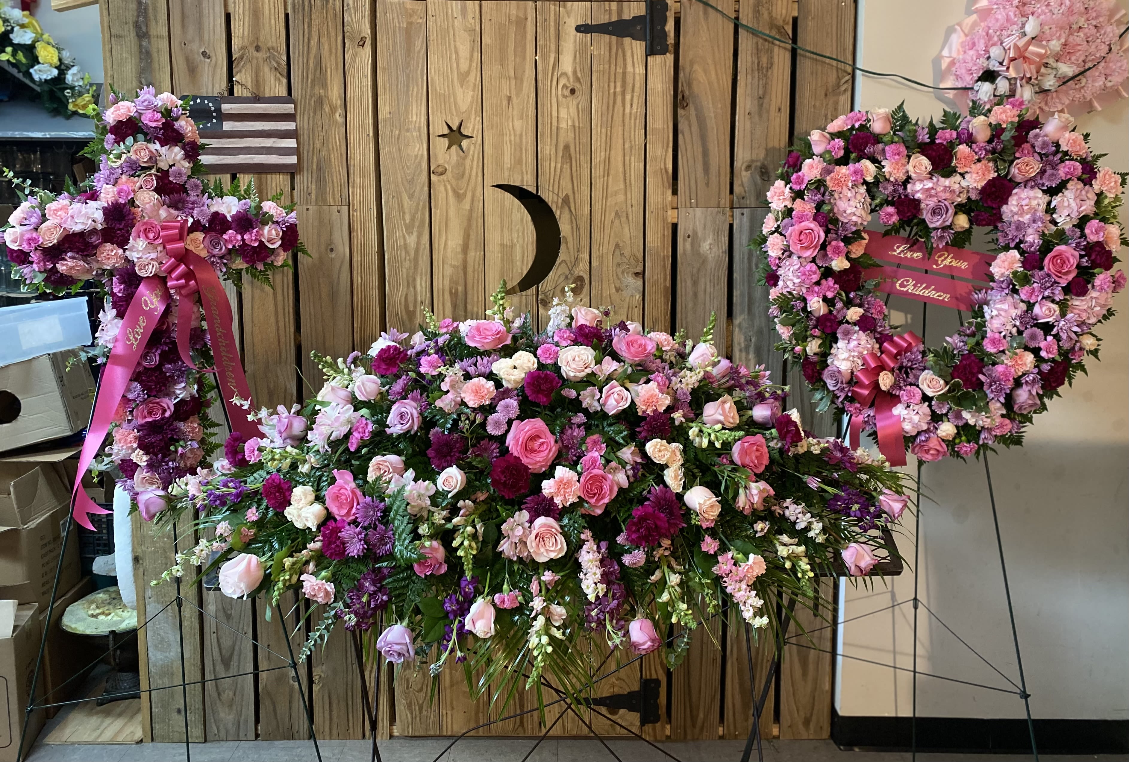 Pink and purple floral funeral display with a heart wreath and cross spray