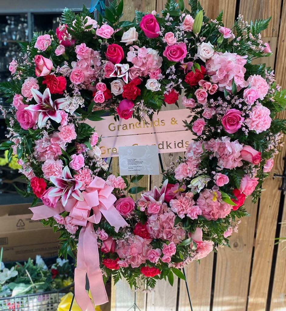 Heart-shaped floral wreath with pink roses, carnations, and lilies on an easel