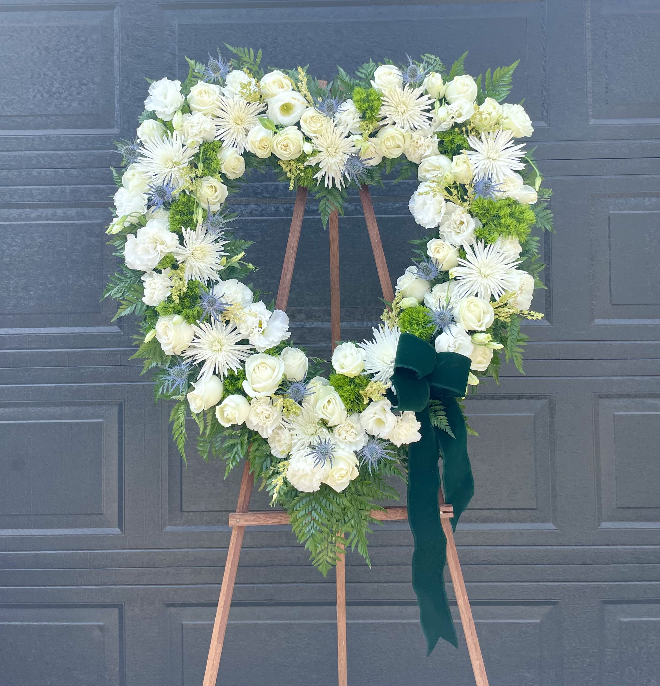 White Forever Heart  - Beautifully arranged open heart in whites and greens to celebrate a loved ones life. Ribbon is optional.  Deluxe and Premium arrangements will include additional flowers giving it a larger size. 