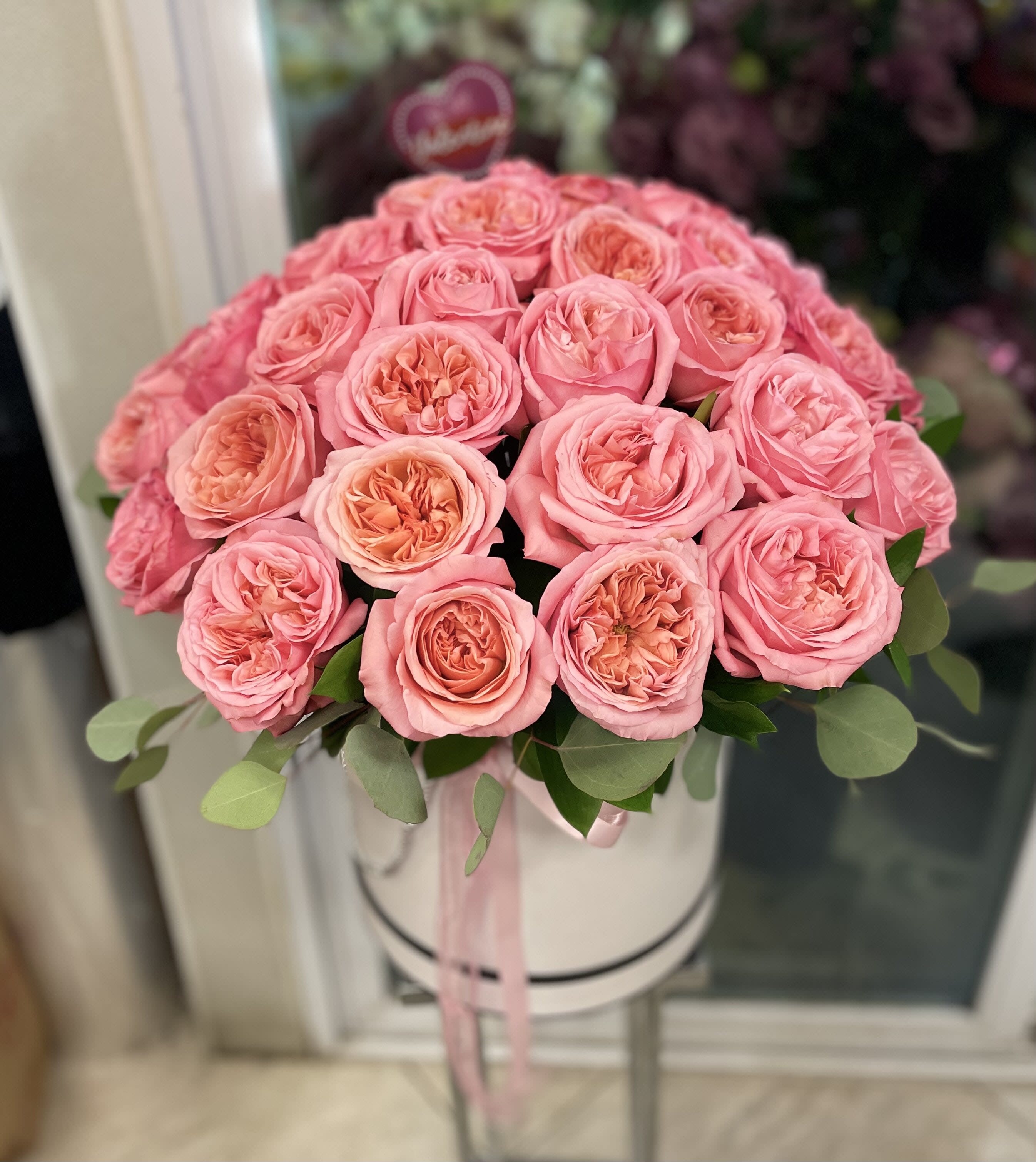 Pink roses arranged in a round white hat box with a ribbon