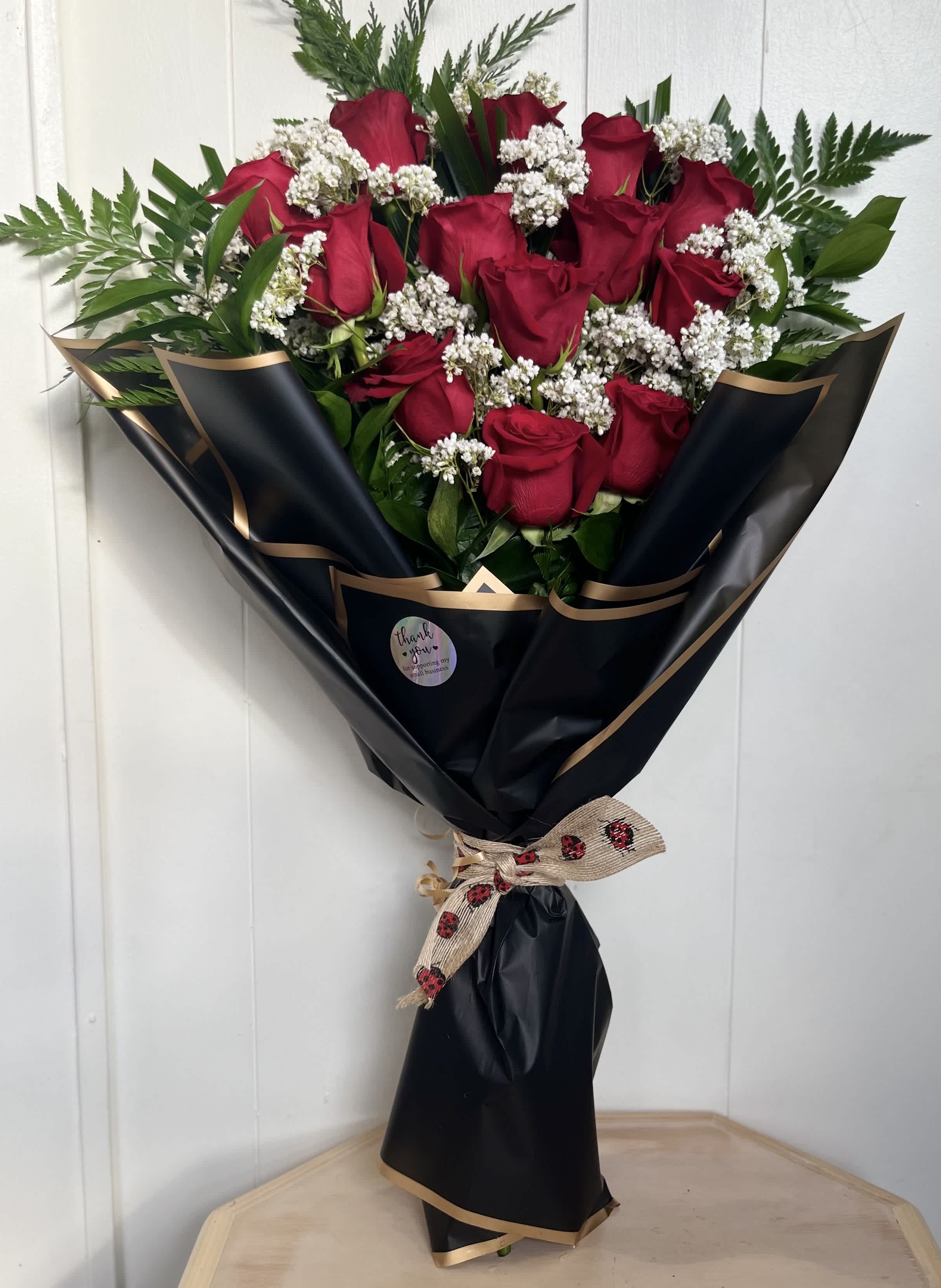 Bouquet of red roses with white filler flowers wrapped in black paper