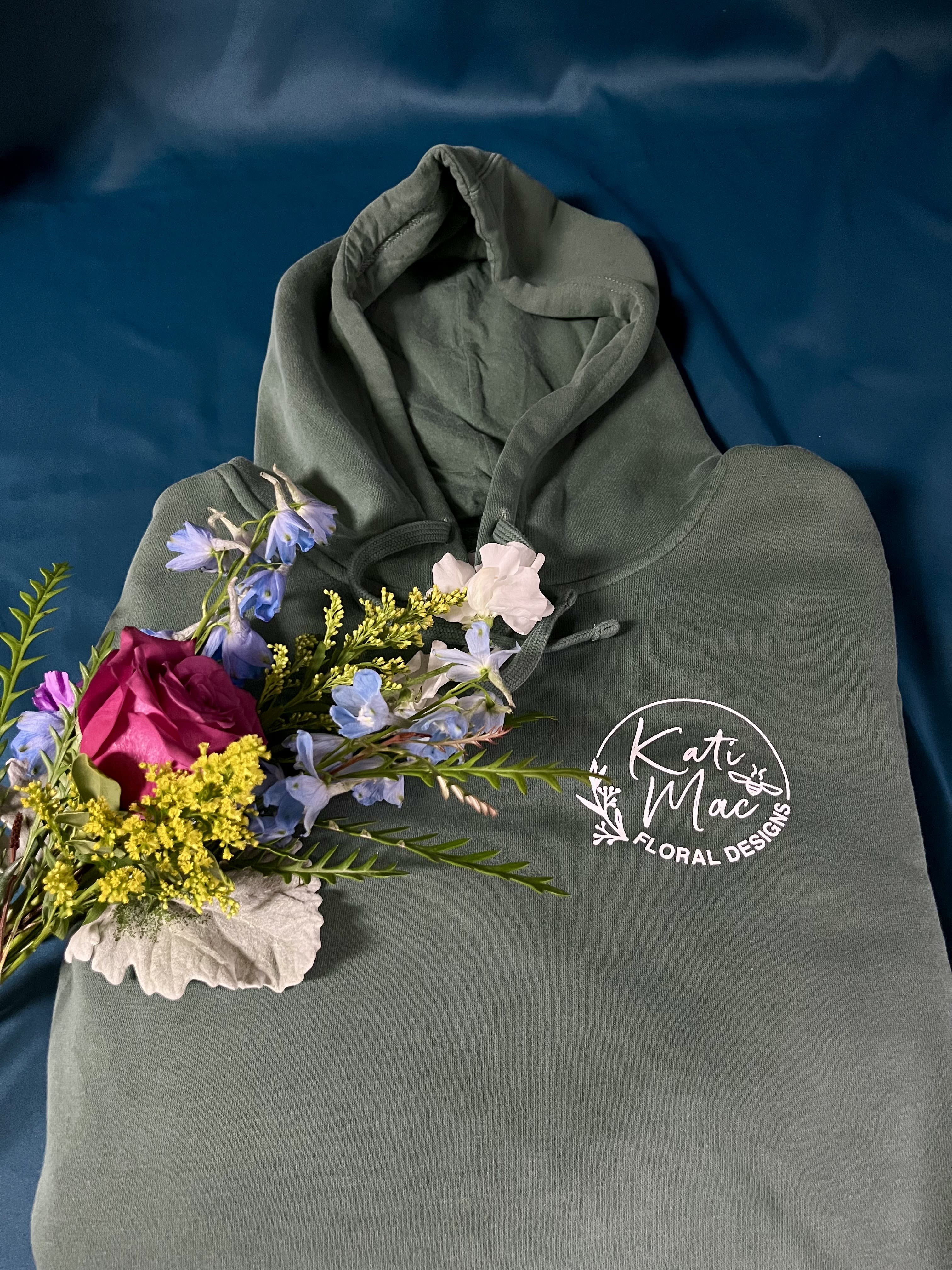 Green logo hoodie with a small colorful floral spray on a dark blue background
