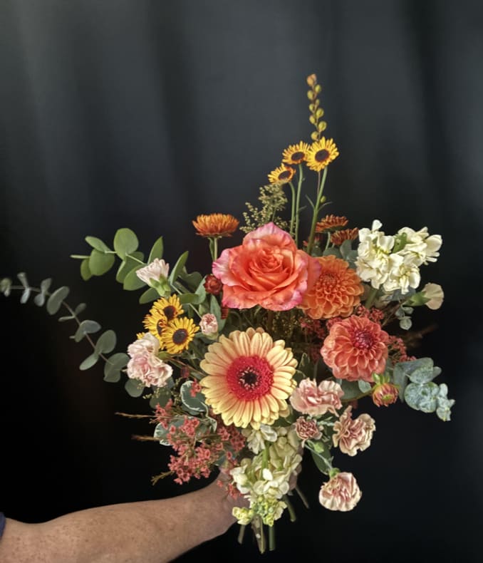 Handheld bouquet with orange and yellow flowers against a dark background.