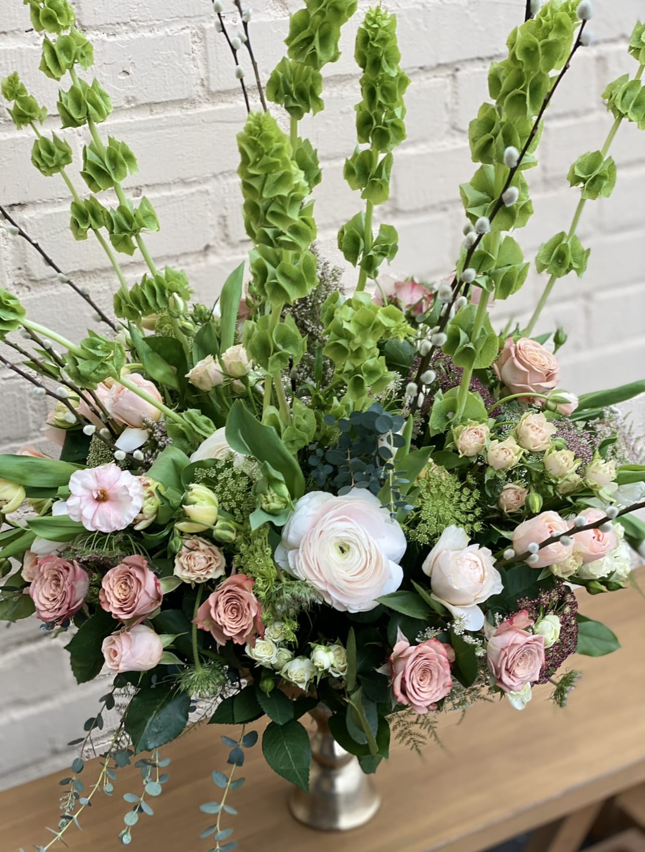 Tall bouquet of pink and white roses with green blooms in a silver vase