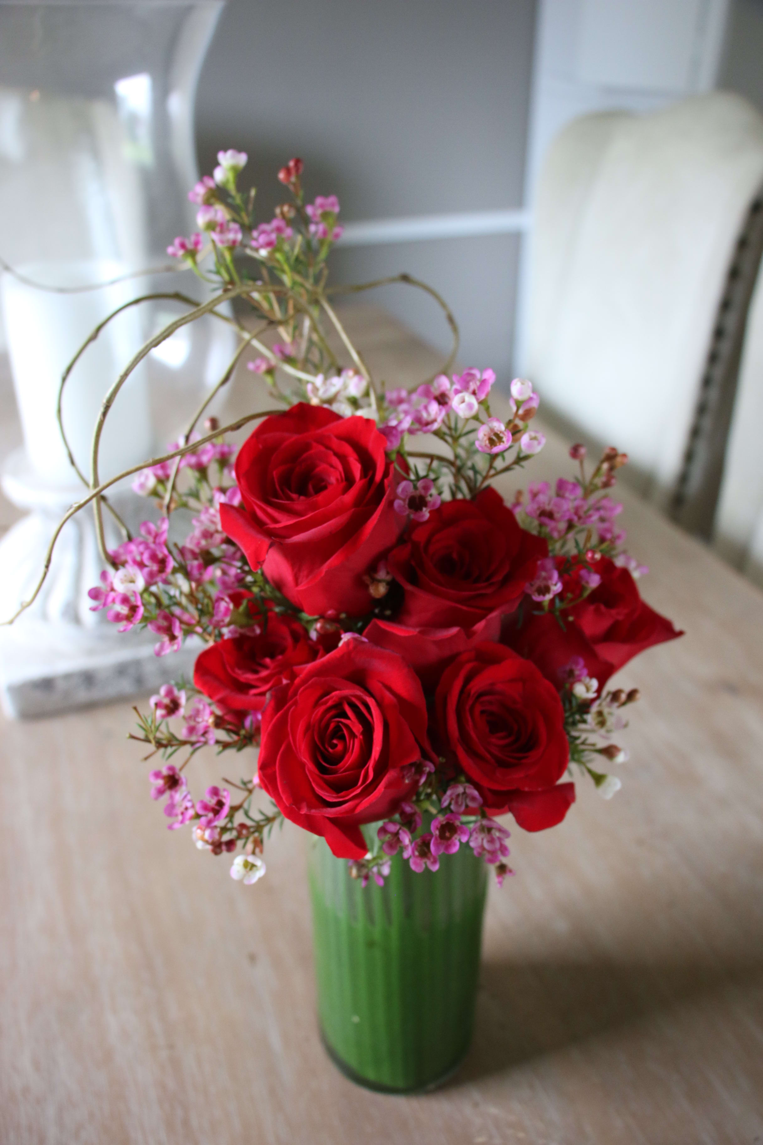 Red roses arranged in a green glass vase with small pink filler flowers