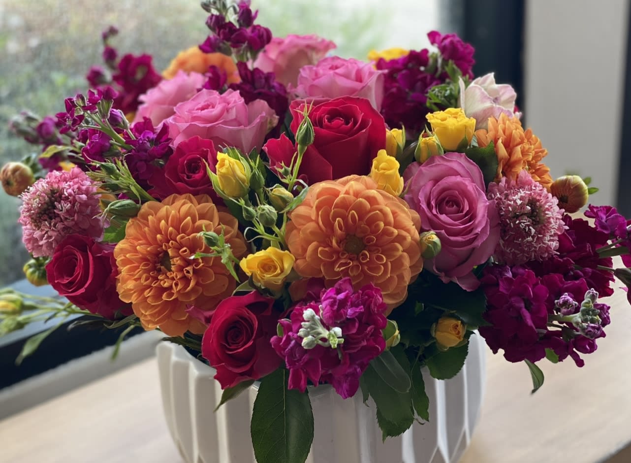 Mixed bouquet of roses, dahlias, and purple blooms in a white vase