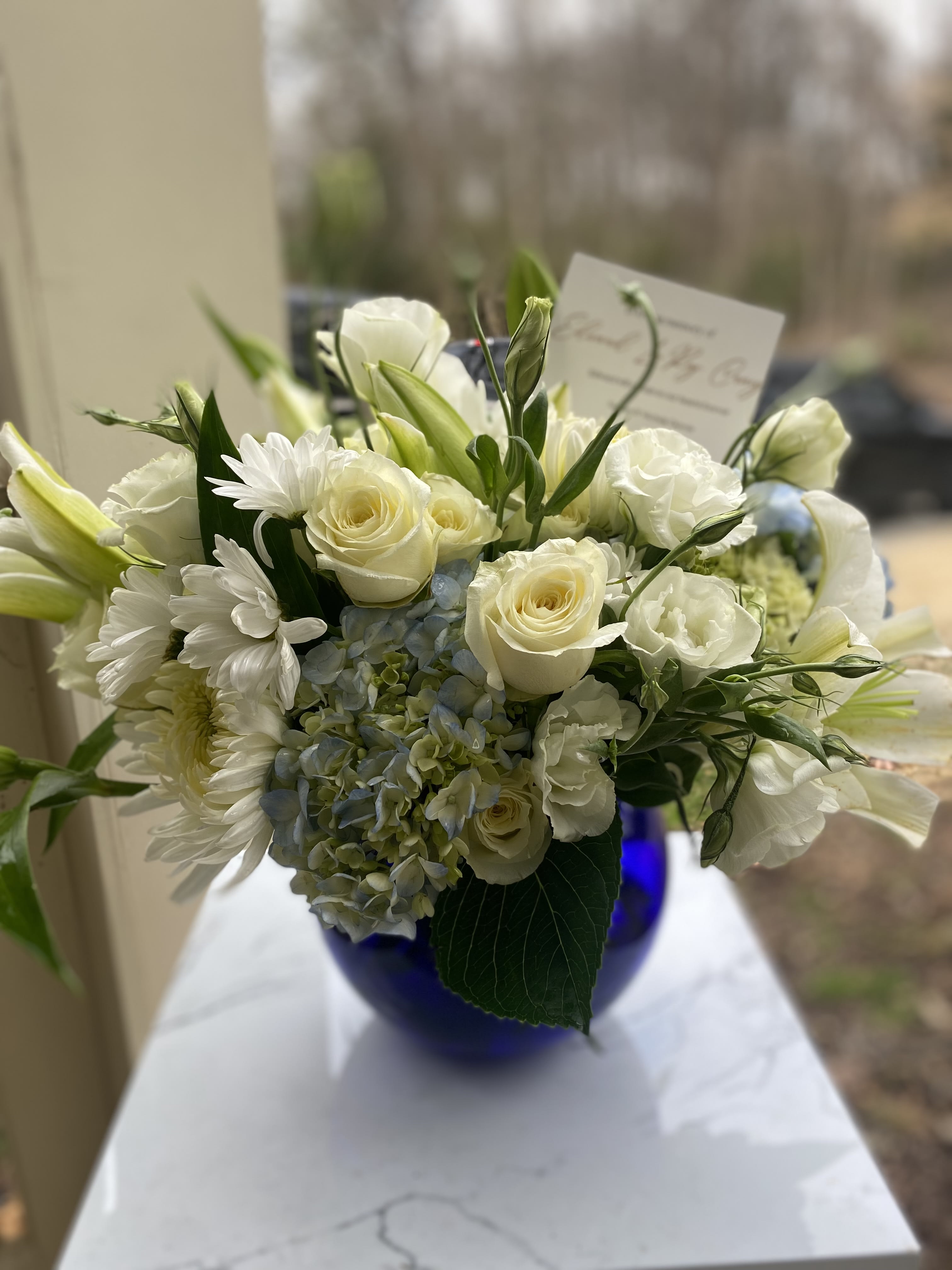 White roses, lilies, daisies, and blue hydrangea in a cobalt vase