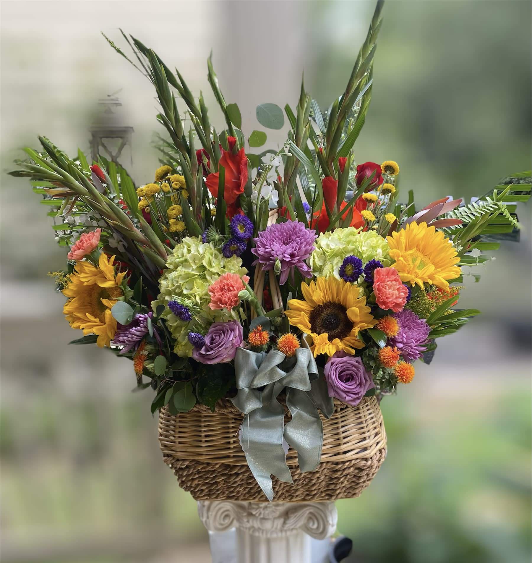 Rainey Basket - Want to WOW or Welcome with florals? Let us create a stunning  expression of mixed colorful florals in a basket BIGGER than life! Imagine this floral basket on top of a whiskey barrel welcoming wedding guest? Or imagine it’s positioned on a foyer table welcoming loved ones to a celebration of life. Let us wake up the atmosphere with our special curated Rainey Basket for special events!