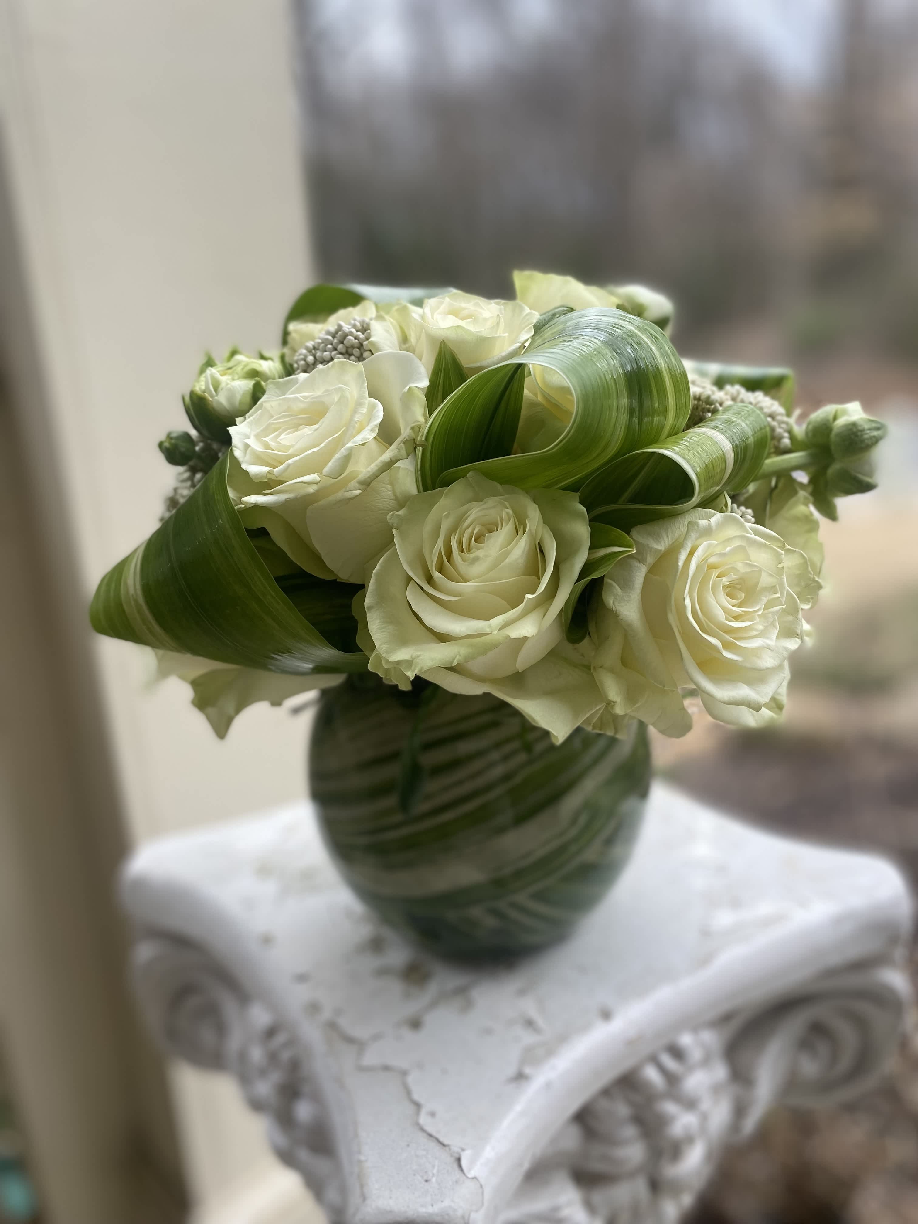 Riverstone - This arrangement is the perfect combination of white/ivory roses with a ribbon of greenery! This arrangement can be duplicated in several colors upon request.  5/6 inch vase is standard. Standard will also have 6-9 roses 8/10 vase will be the Premium. Premium will also have 12-15 roses 