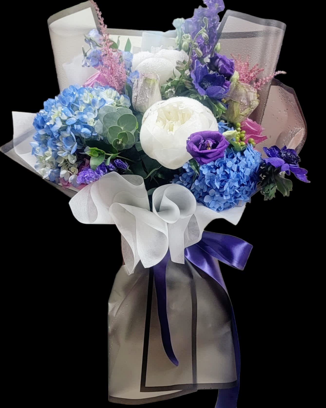 Bouquet of blue, purple, and white flowers wrapped in sheer paper