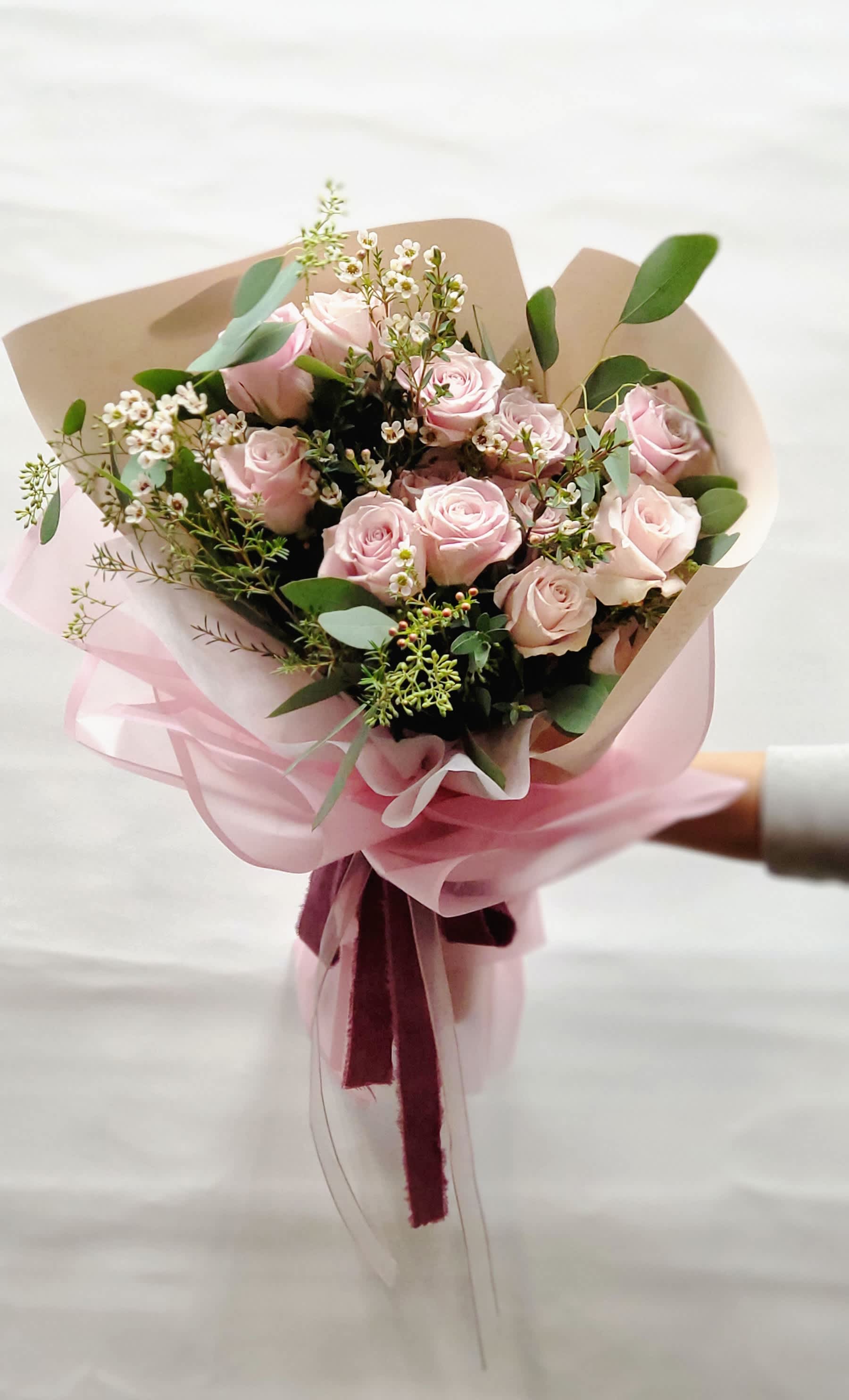 Bouquet of pale pink roses with small white filler flowers and pink wrapping