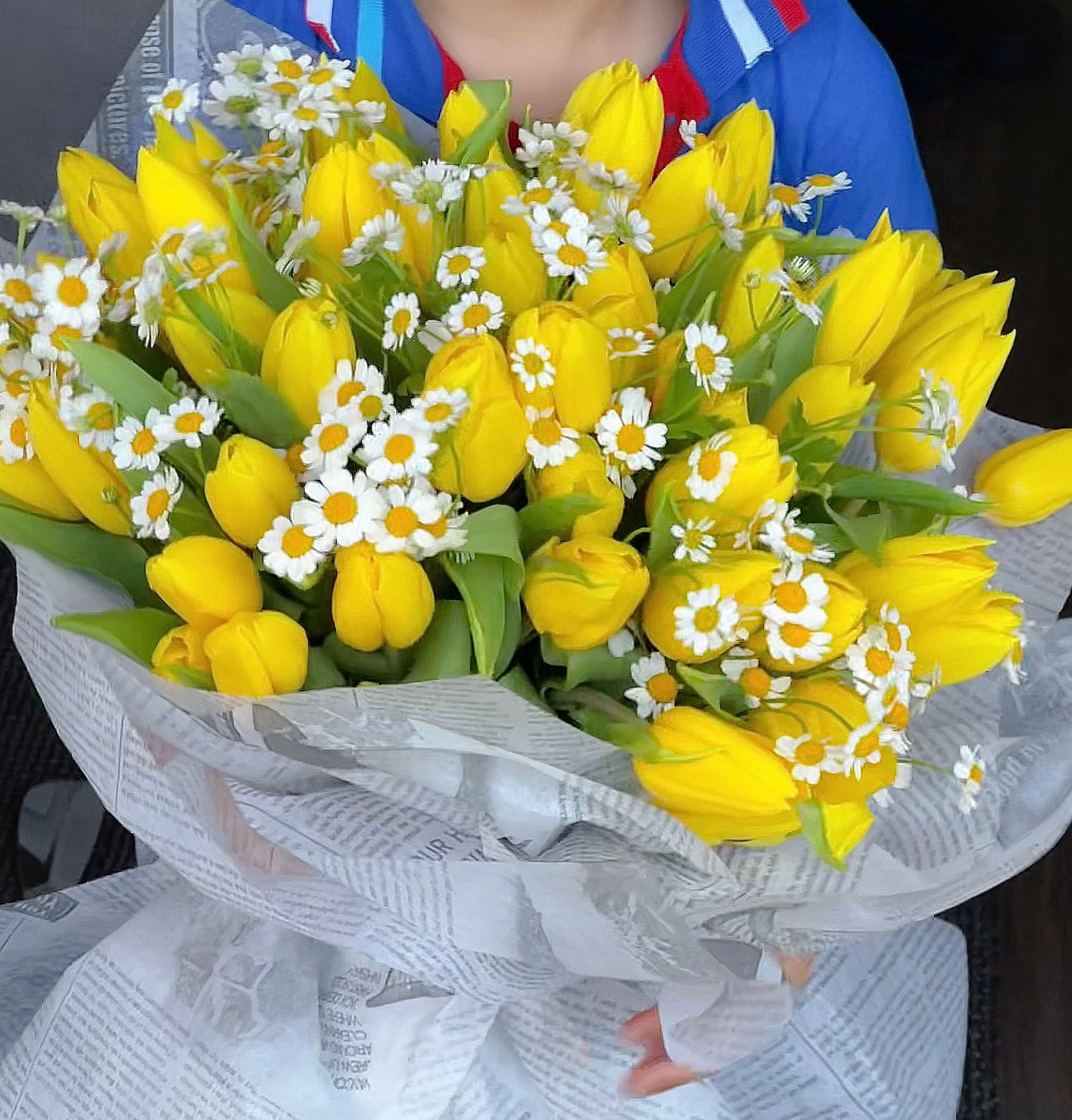 Bouquet of yellow tulips and small white daisies wrapped in paper