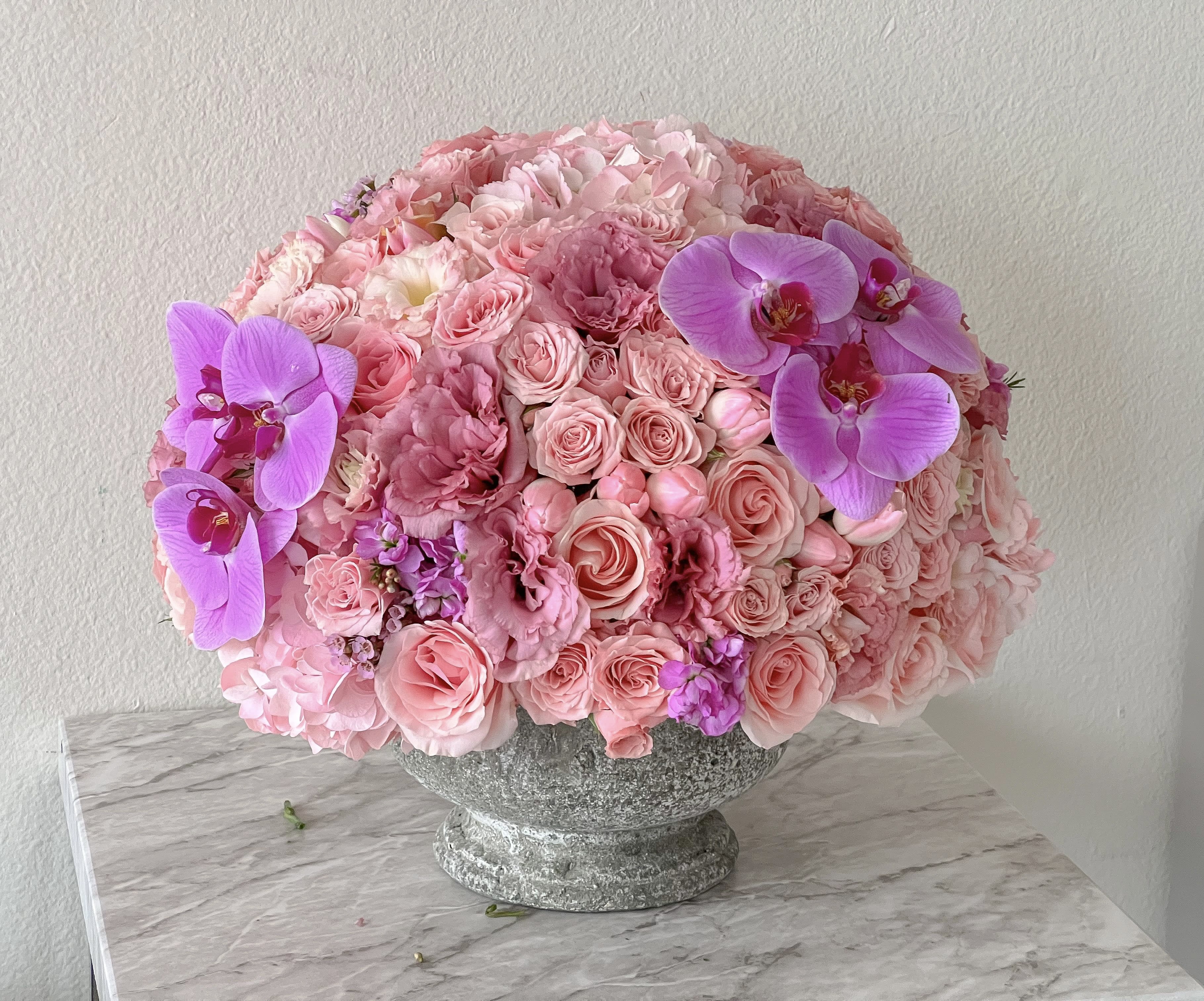 Pink rose and orchid arrangement in a stone pedestal vase