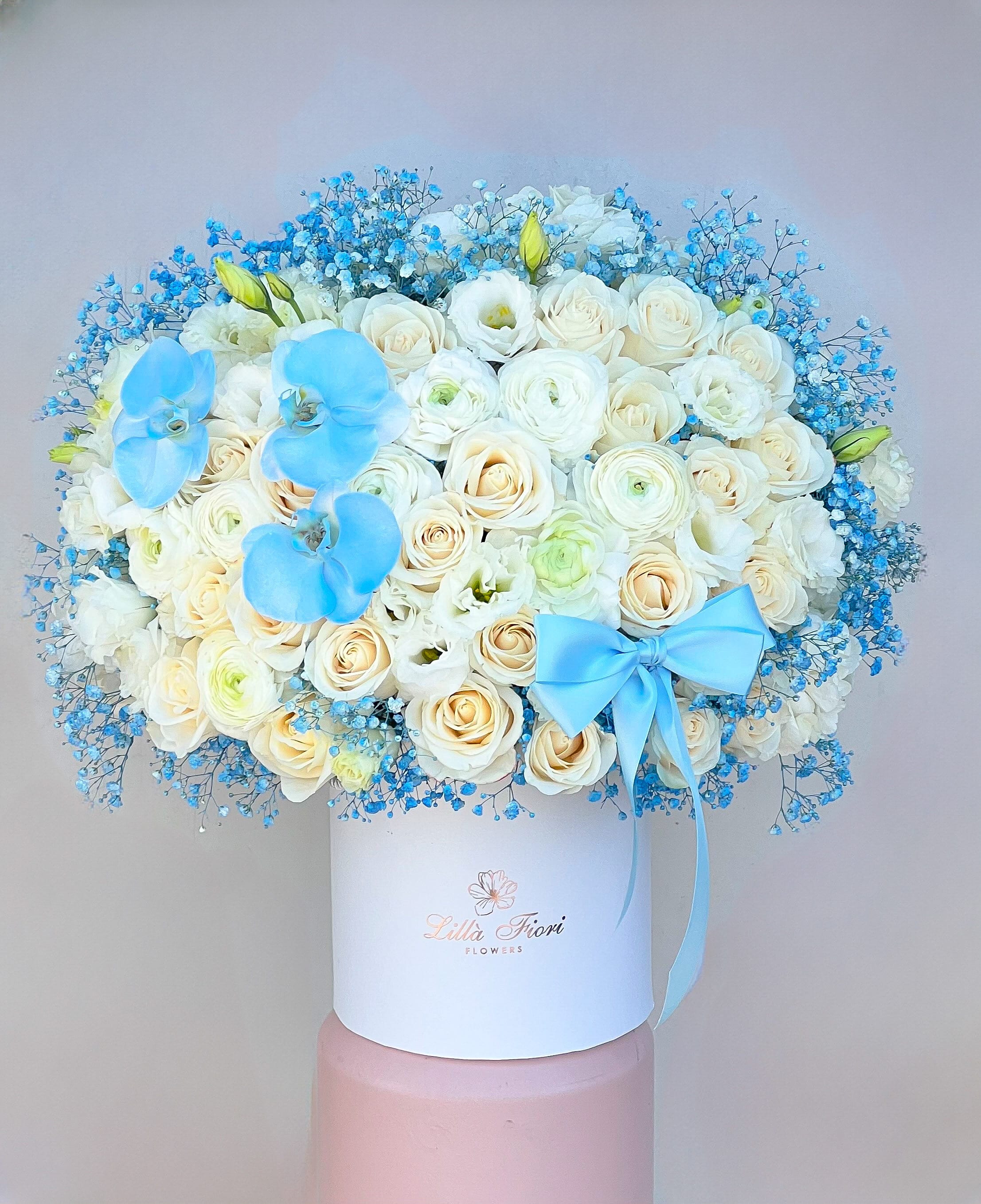 White rose bouquet with blue orchids and a blue ribbon in a white box