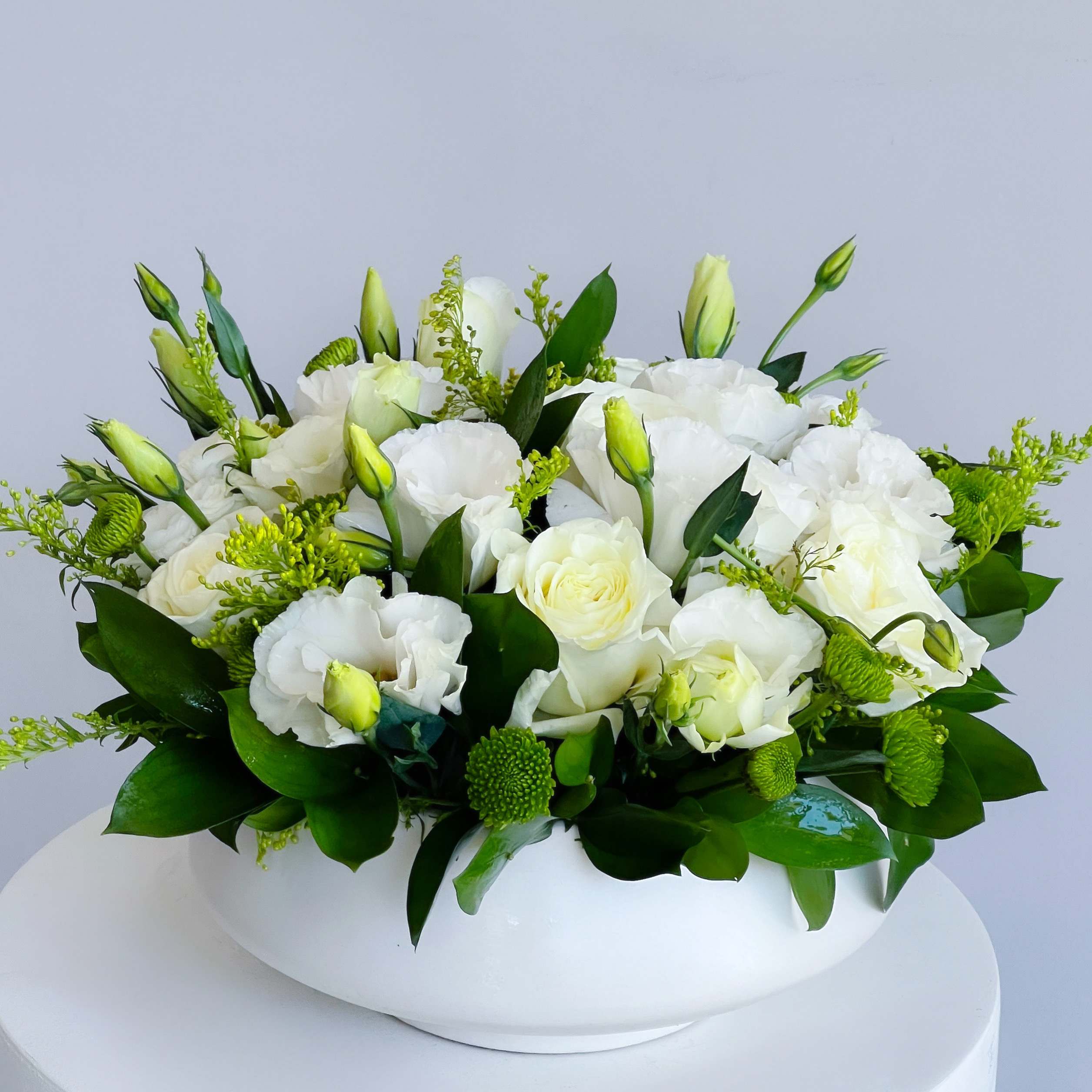 White floral arrangement in a low white vase with green accents