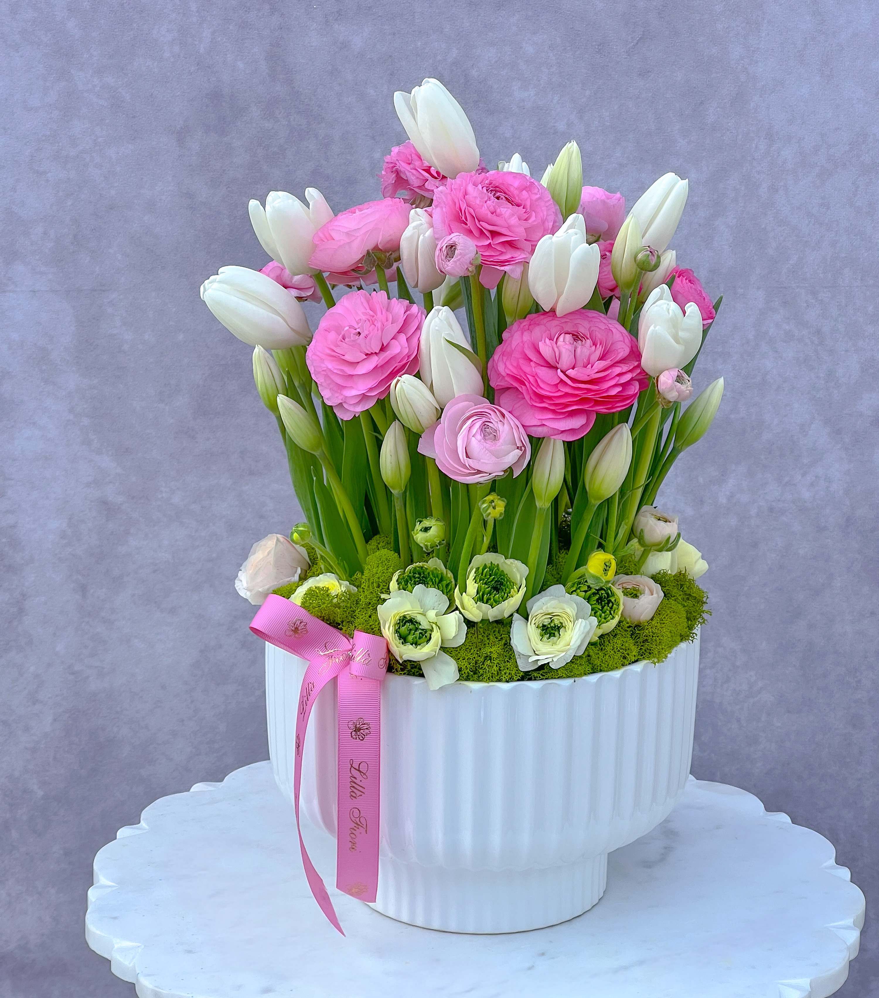 Pink and white flowers arranged in a white vase with a pink ribbon