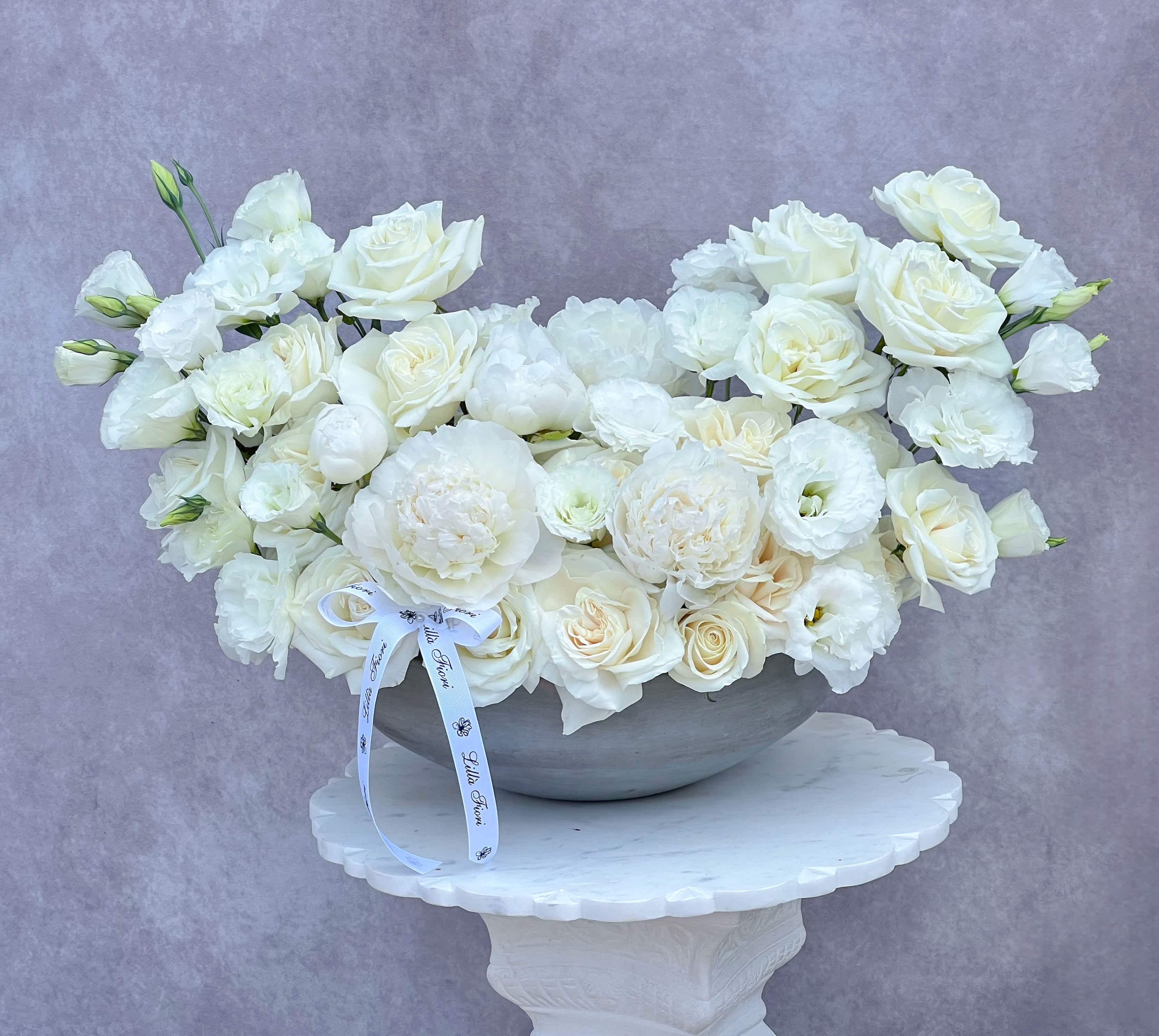 White roses and lisianthus arranged in a gray bowl on a pedestal
