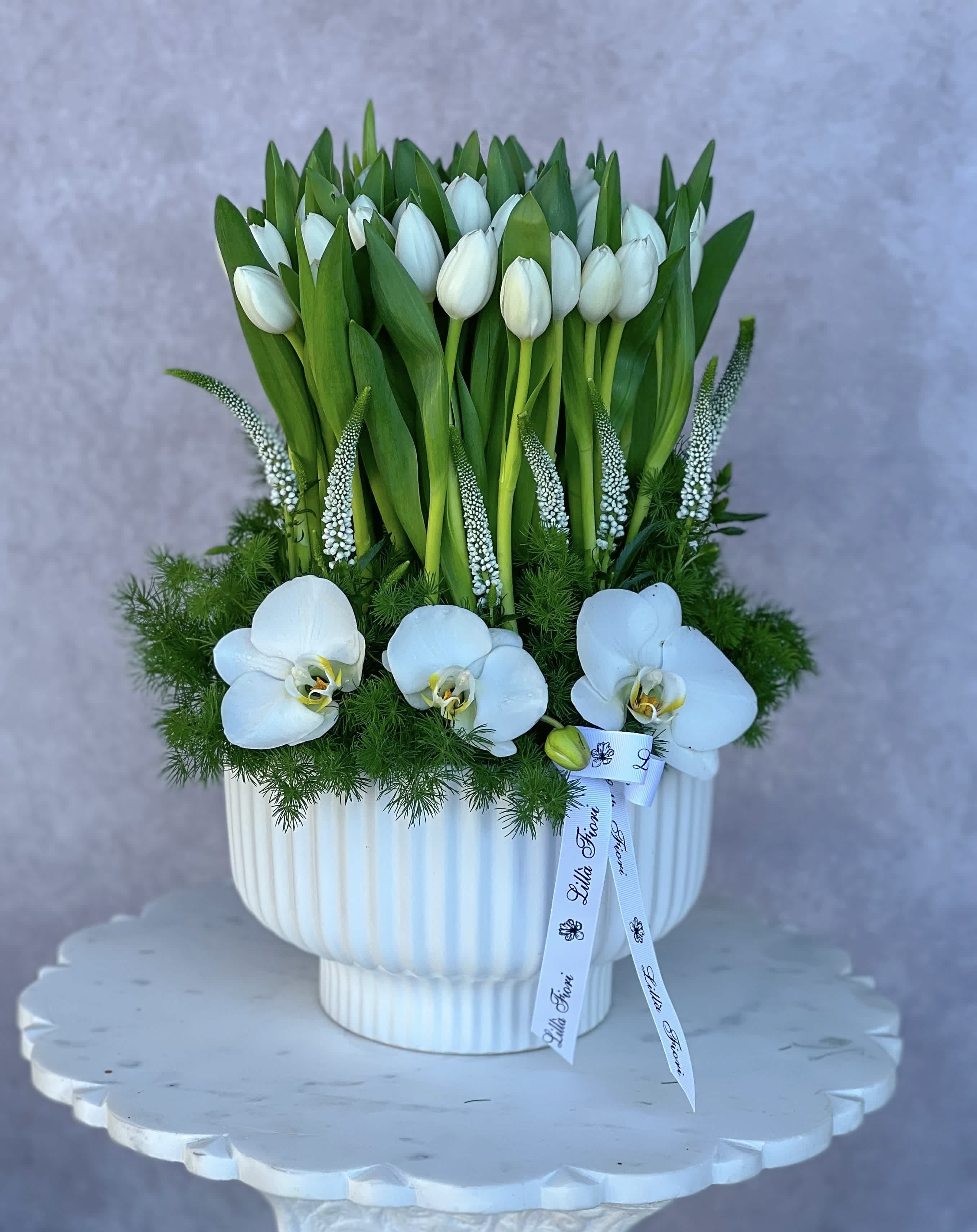 White tulips and orchids arranged in a white pedestal vase