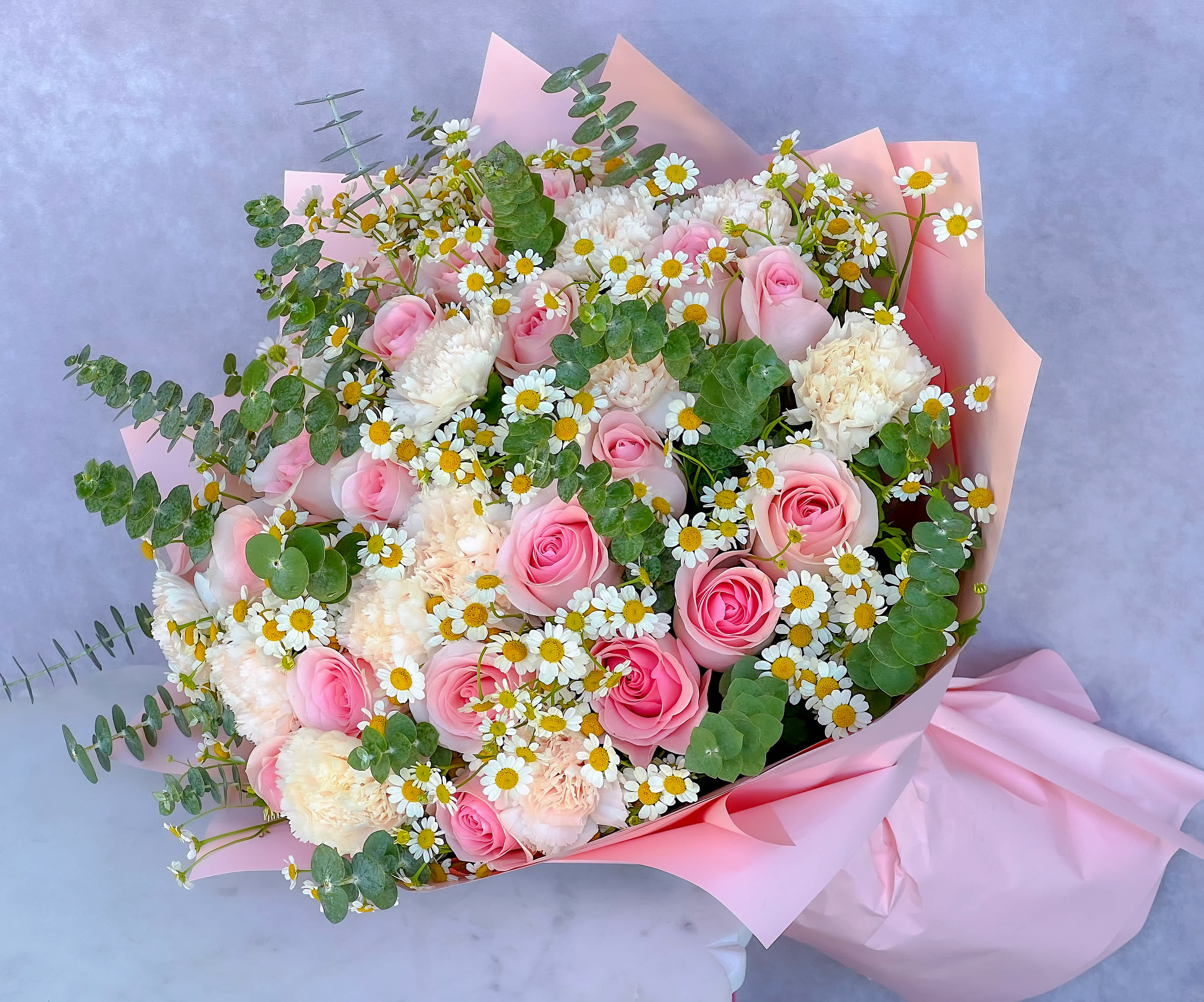 Bouquet of pink roses, white carnations, and daisies wrapped in pink paper