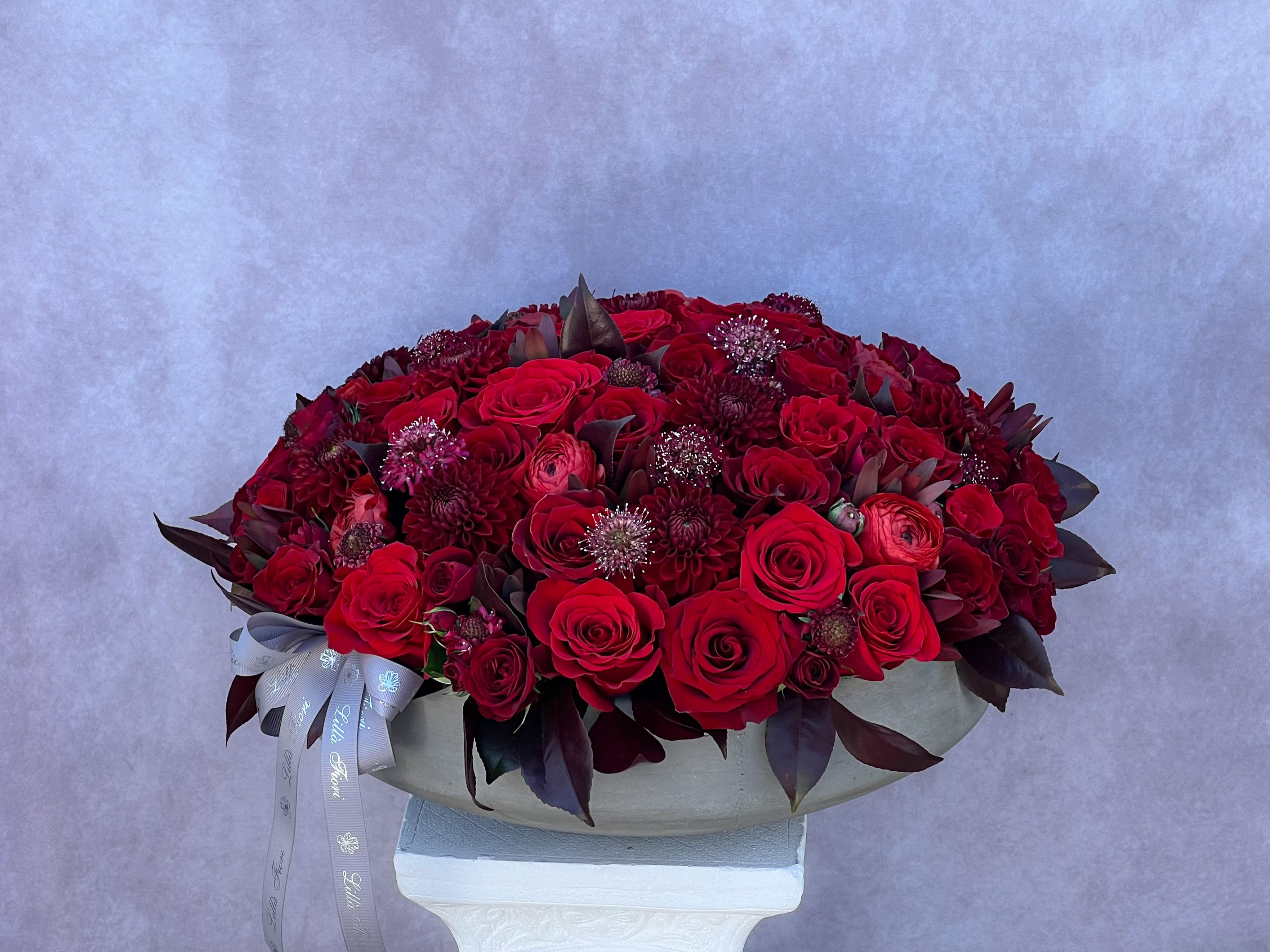 Large red rose arrangement in a shallow white container with a ribbon