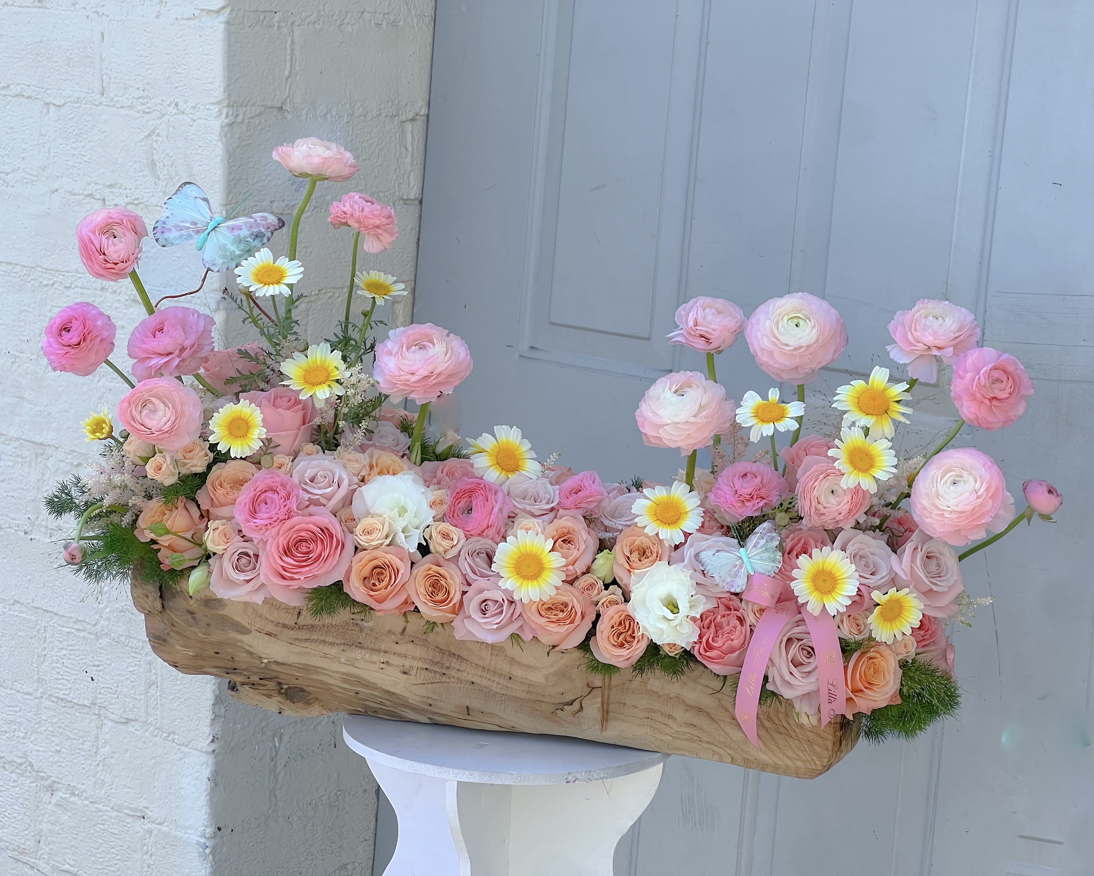 Pink and peach flower arrangement in a wooden container with daisies and butterflies