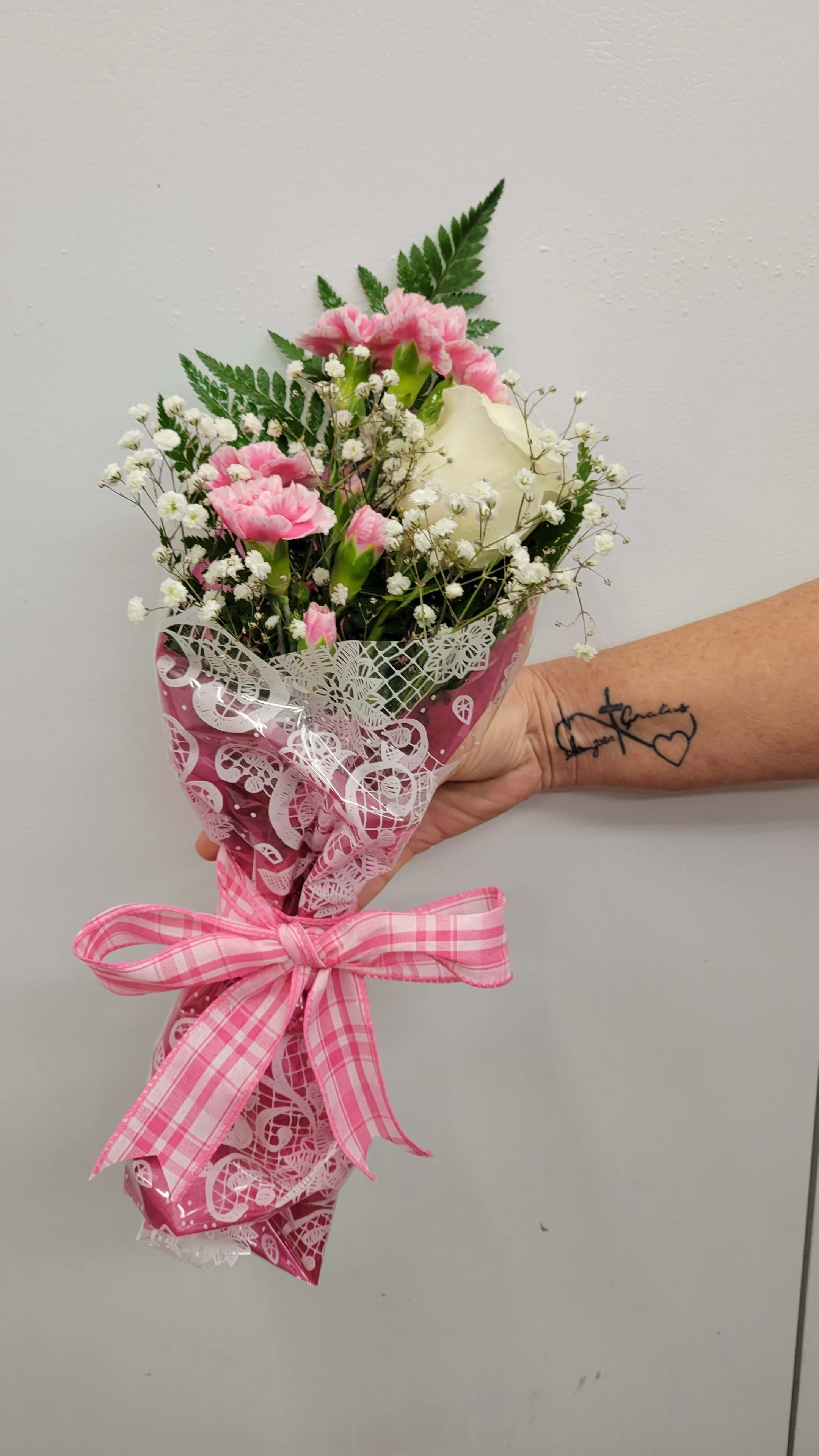 Pink carnations and a white rose in a wrapped bouquet with a pink ribbon