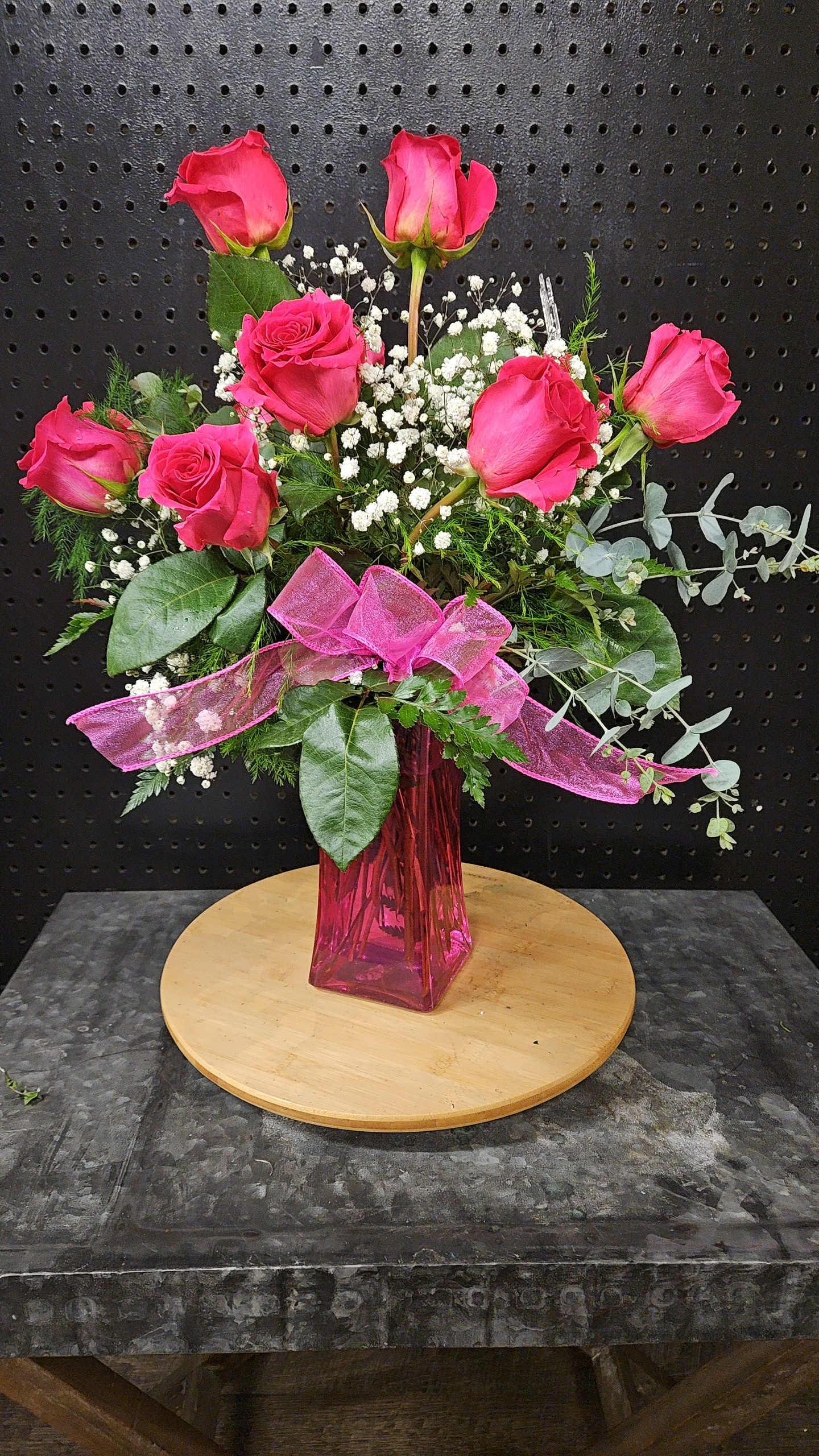 Pink roses arranged in a tall pink vase with baby's breath and ribbon