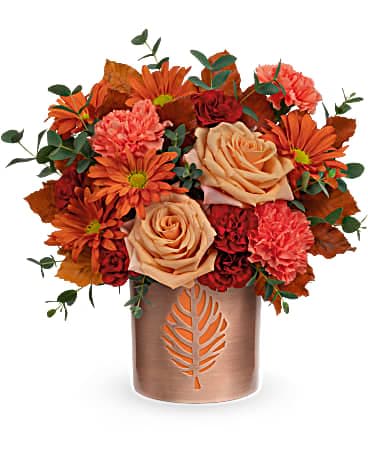 Teleflora's Lovely Leaves Bouquet - Bursting with autumnal roses, this gorgeous copper-finished metal keepsake with delicate cutout leaf motif doubles as a vase and a candleholder. This arrangement includes light orange roses, orange carnations, miniature maroon carnations, bronze daisy spray chrysanthemums, parvifolia eucalyptus and brown copper beech. Delivered in a Lovely Leaves Cylinder.