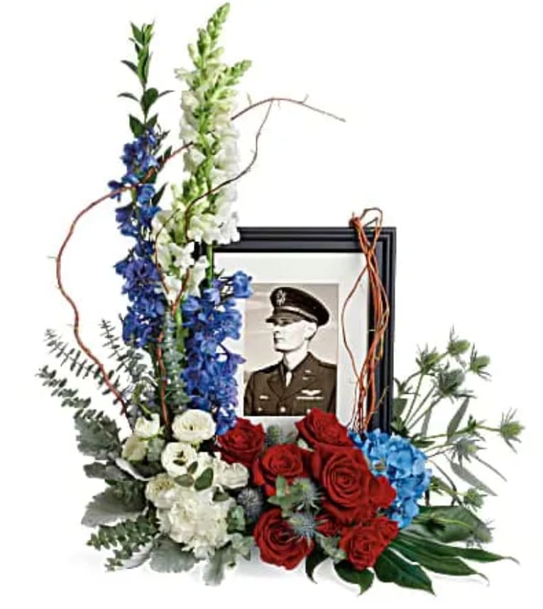 Floral tribute with a framed military portrait and red, white, and blue flowers