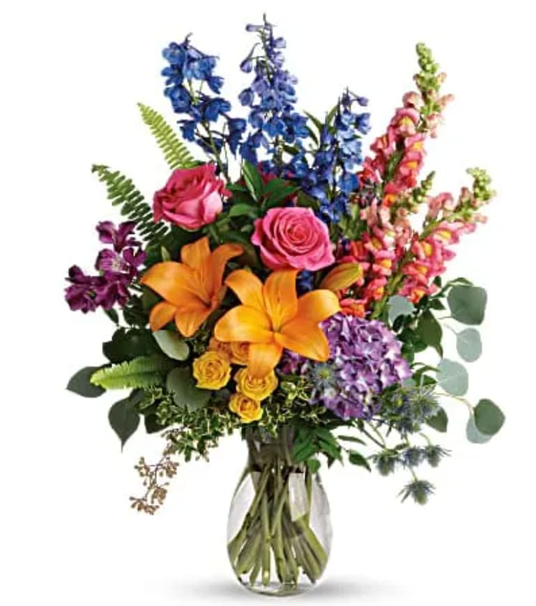 Colorful mixed bouquet in a clear glass vase with roses, lilies, and snapdragons