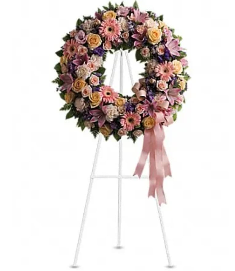 Pastel floral wreath on a white stand with a pink ribbon