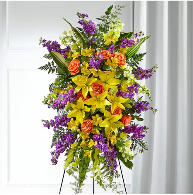 Tall standing floral spray with yellow lilies, orange roses, and purple flowers
