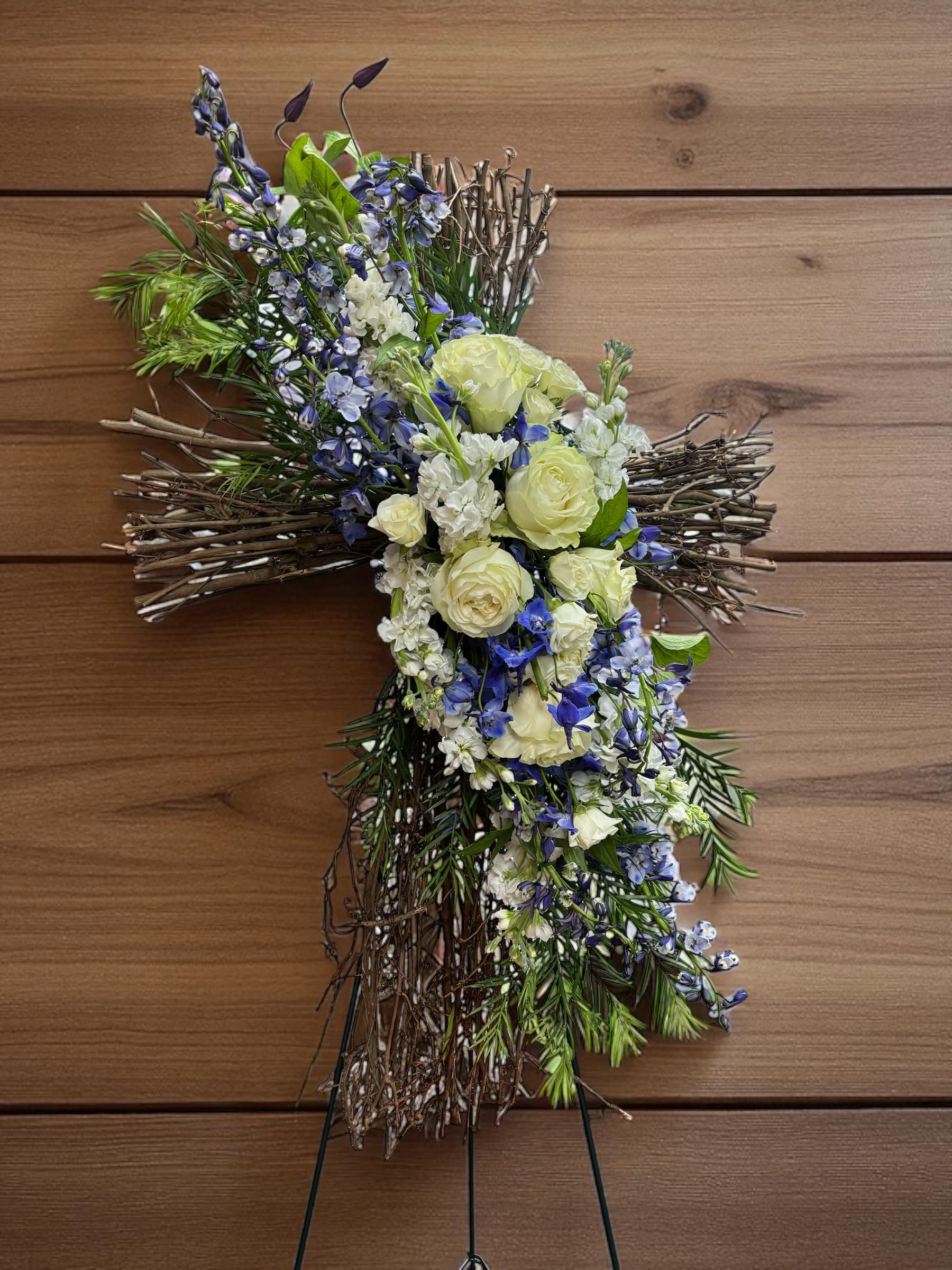 Cross-shaped floral tribute with white and blue flowers on a twig base
