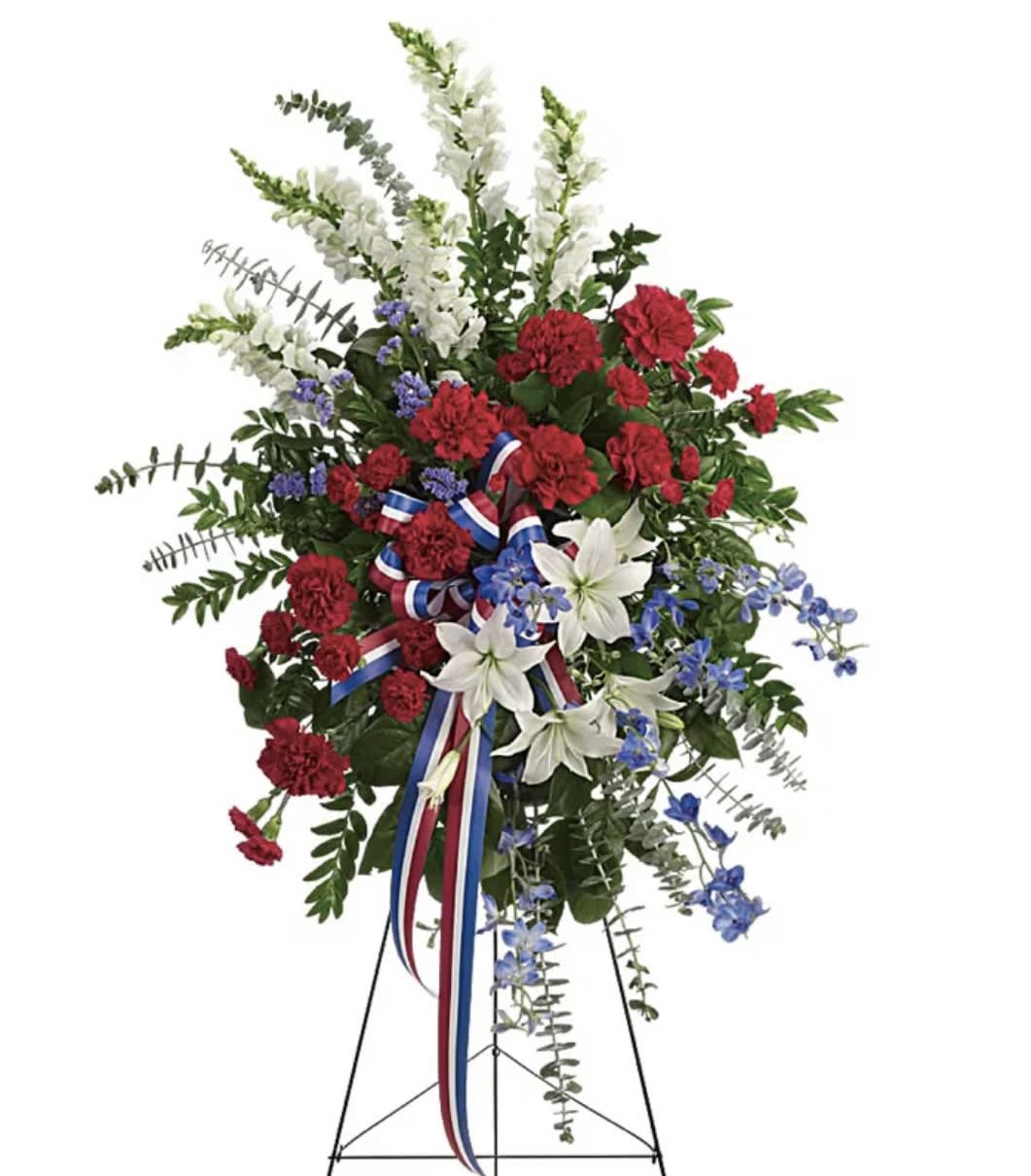 Standing floral spray with red carnations, white lilies, and blue flowers on a tripod stand