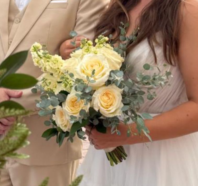 Bridal hand-tied bouquet of pale yellow roses and cream flowers with soft greenery, held by a bride in white.