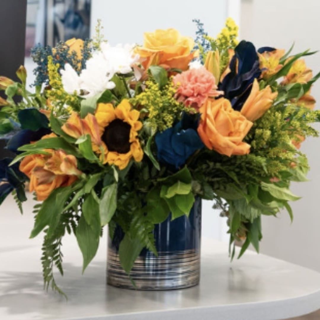 Mixed bouquet of roses, sunflowers, and lilies in a blue vase