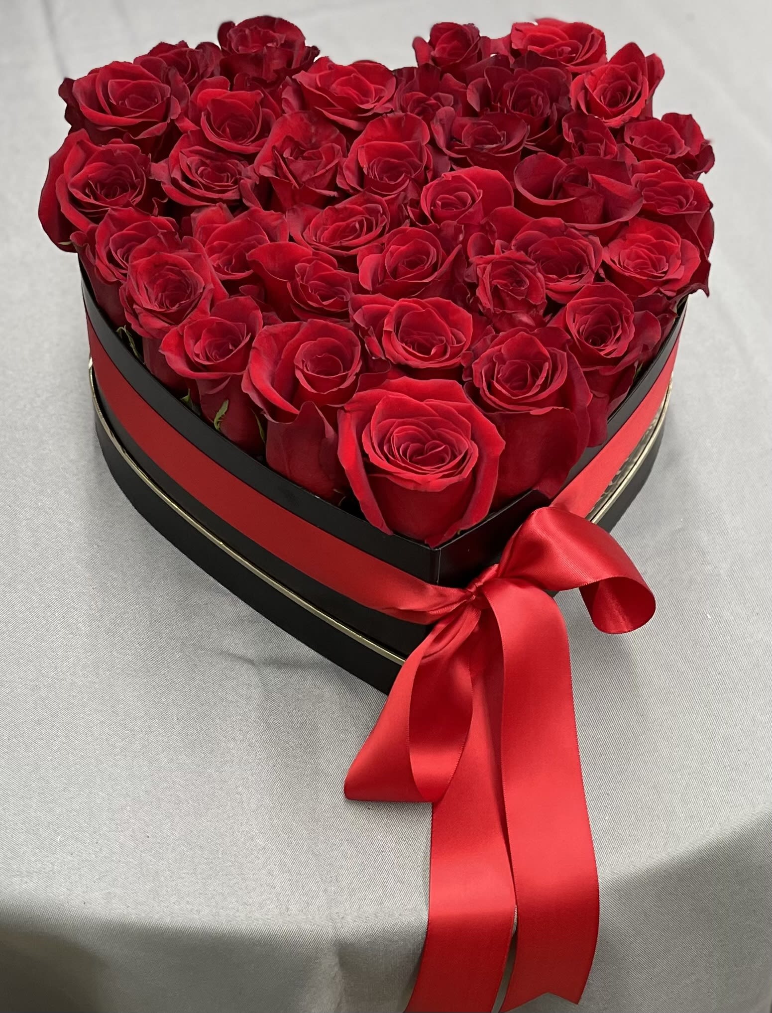 Heart-shaped box filled with red roses and a red satin ribbon