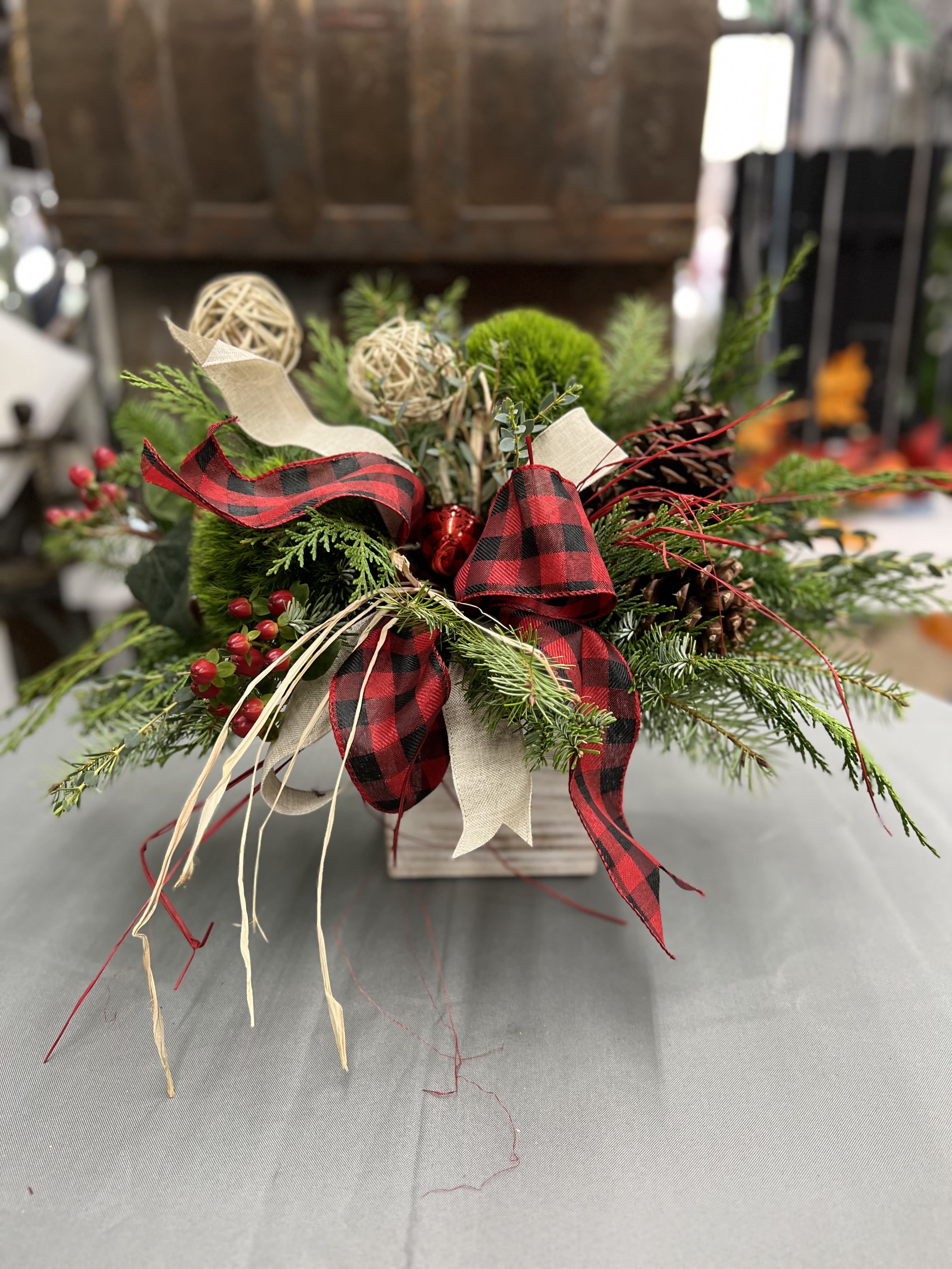 Holiday arrangement of evergreen branches with red plaid ribbon in a wooden container