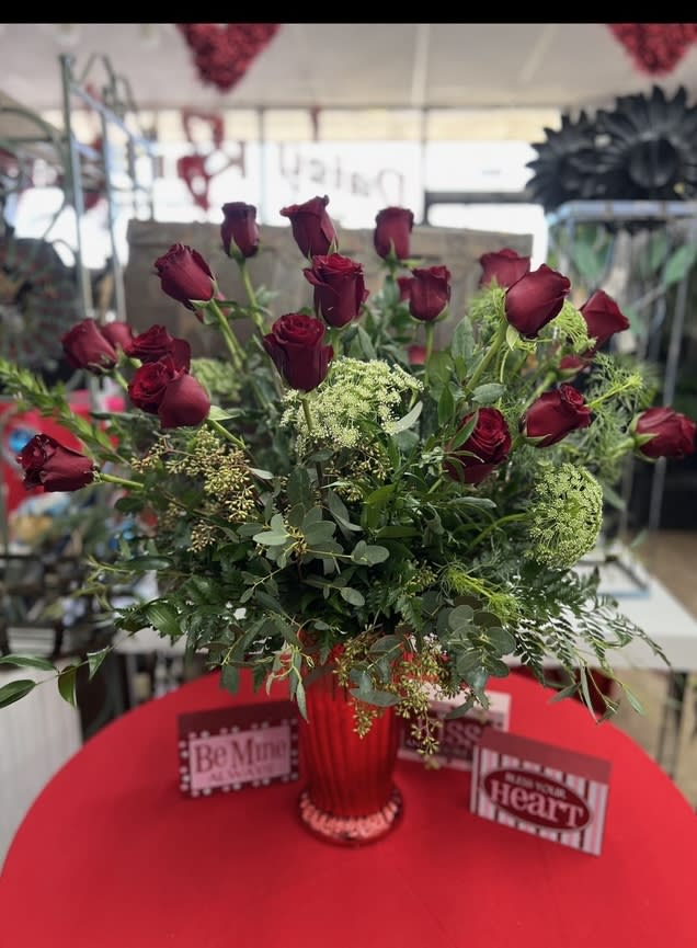 Red roses arranged in a red vase with greenery