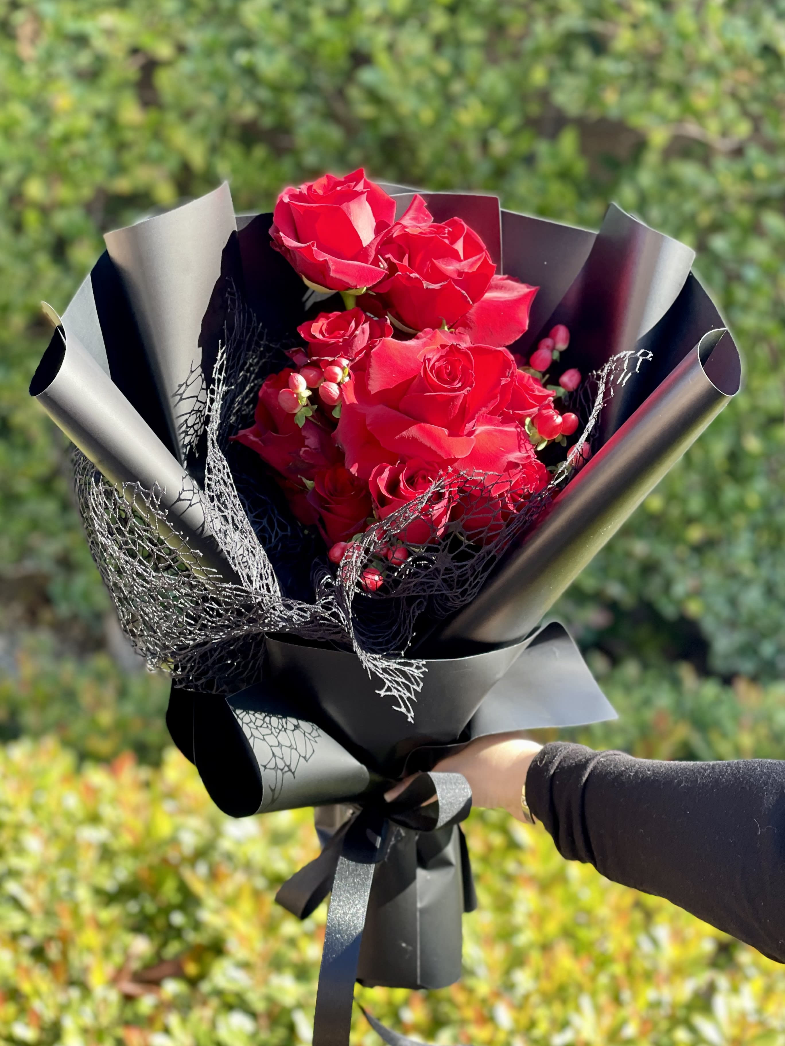 Hand-held bouquet of bright red roses wrapped in matte black paper with black mesh accents