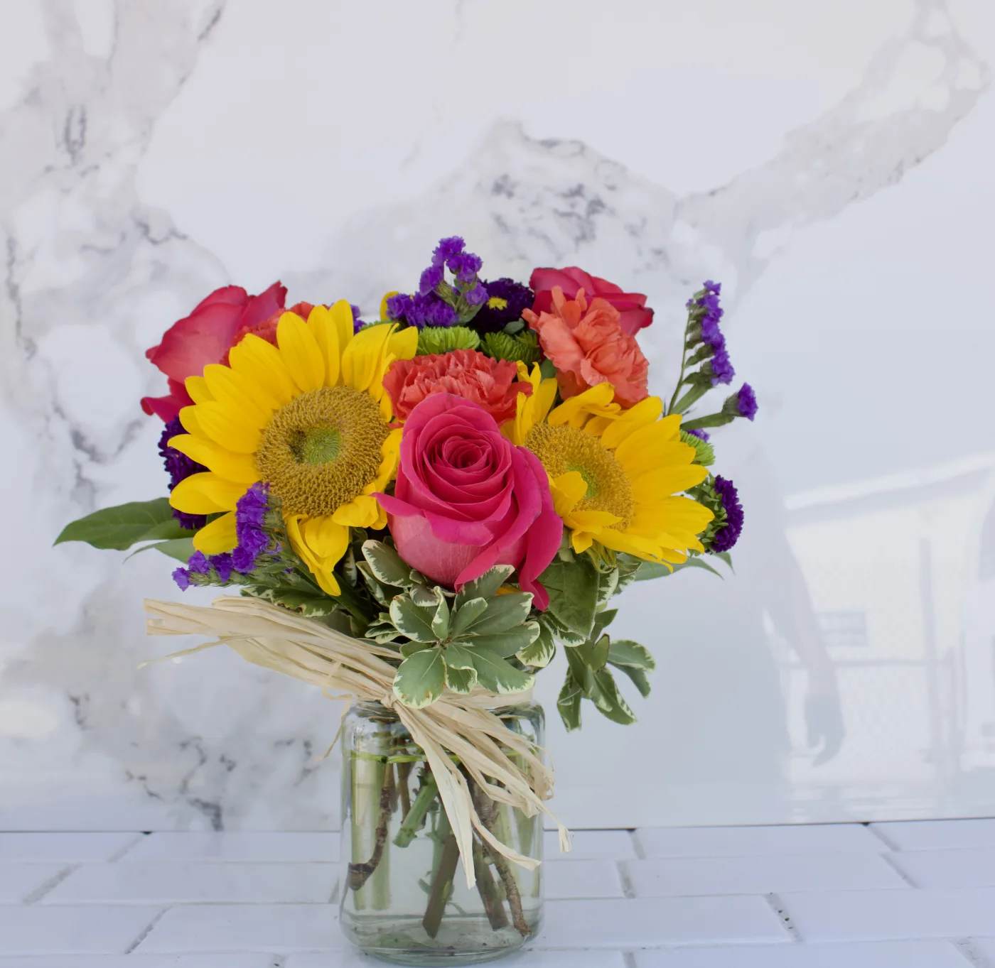 Bouquet of sunflowers, pink roses, and carnations in a glass vase